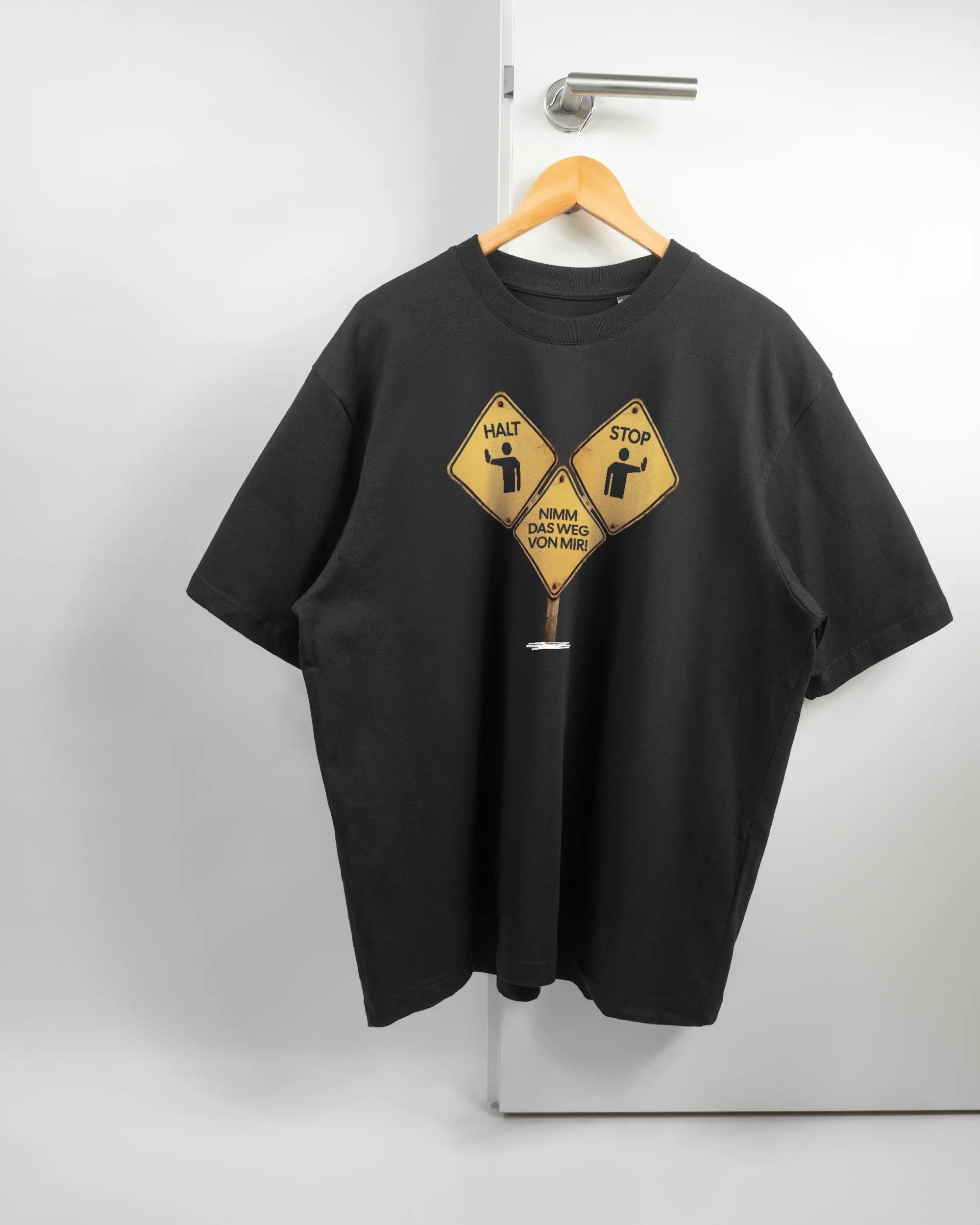 Vorderseite des Basic Unisex T-Shirt Oversized von Maondo mit dem Design Schutzschild in der Farbe Black und in der Größe L auf einem Bügel an der Türklinke aufgehängt