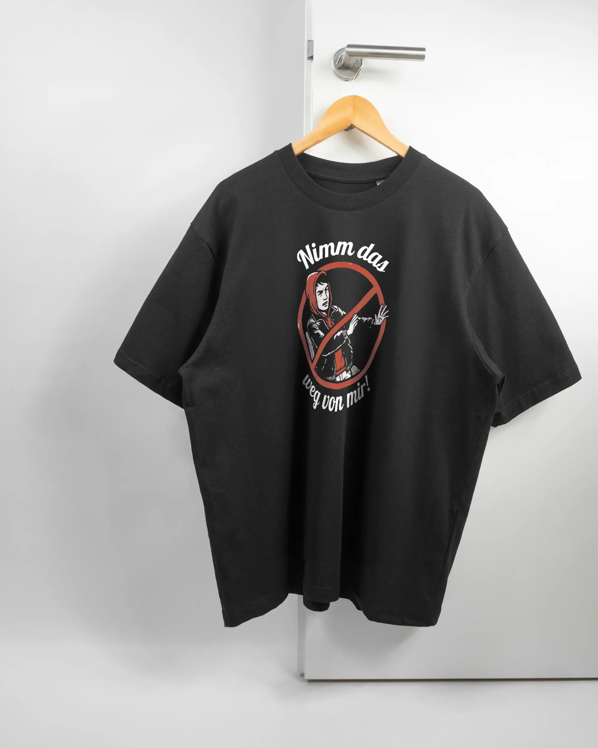 Vorderseite des Basic Unisex T-Shirt Oversized von Maondo mit dem Design Nimm das weg in der Farbe Black und in der Größe L auf einem Bügel an der Türklinke aufgehängt