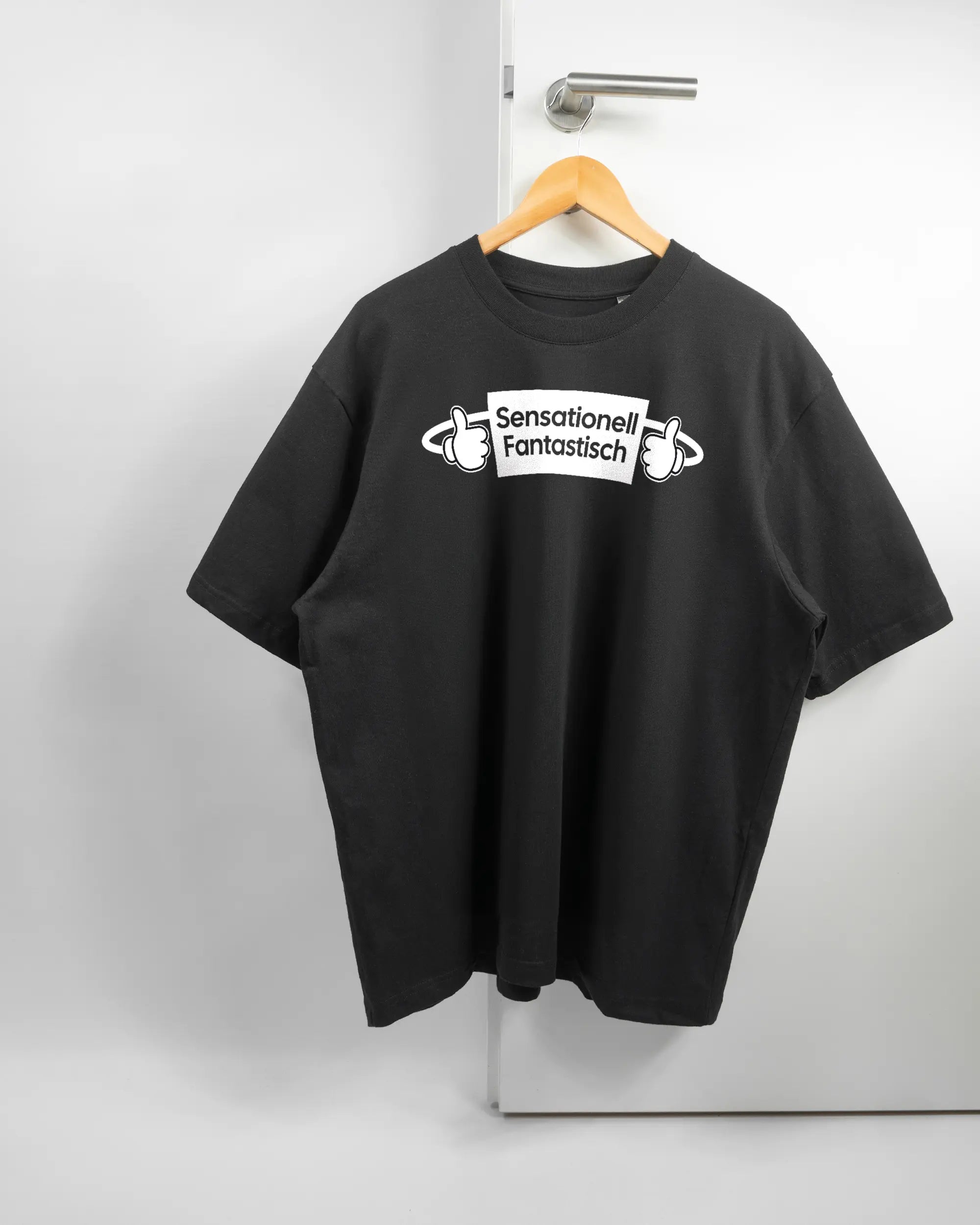 Vorderseite des Basic Unisex T-Shirt Oversized von Maondo mit dem Design Fantastisch in der Farbe Black und in der Größe L auf einem Bügel an der Türklinke aufgehängt