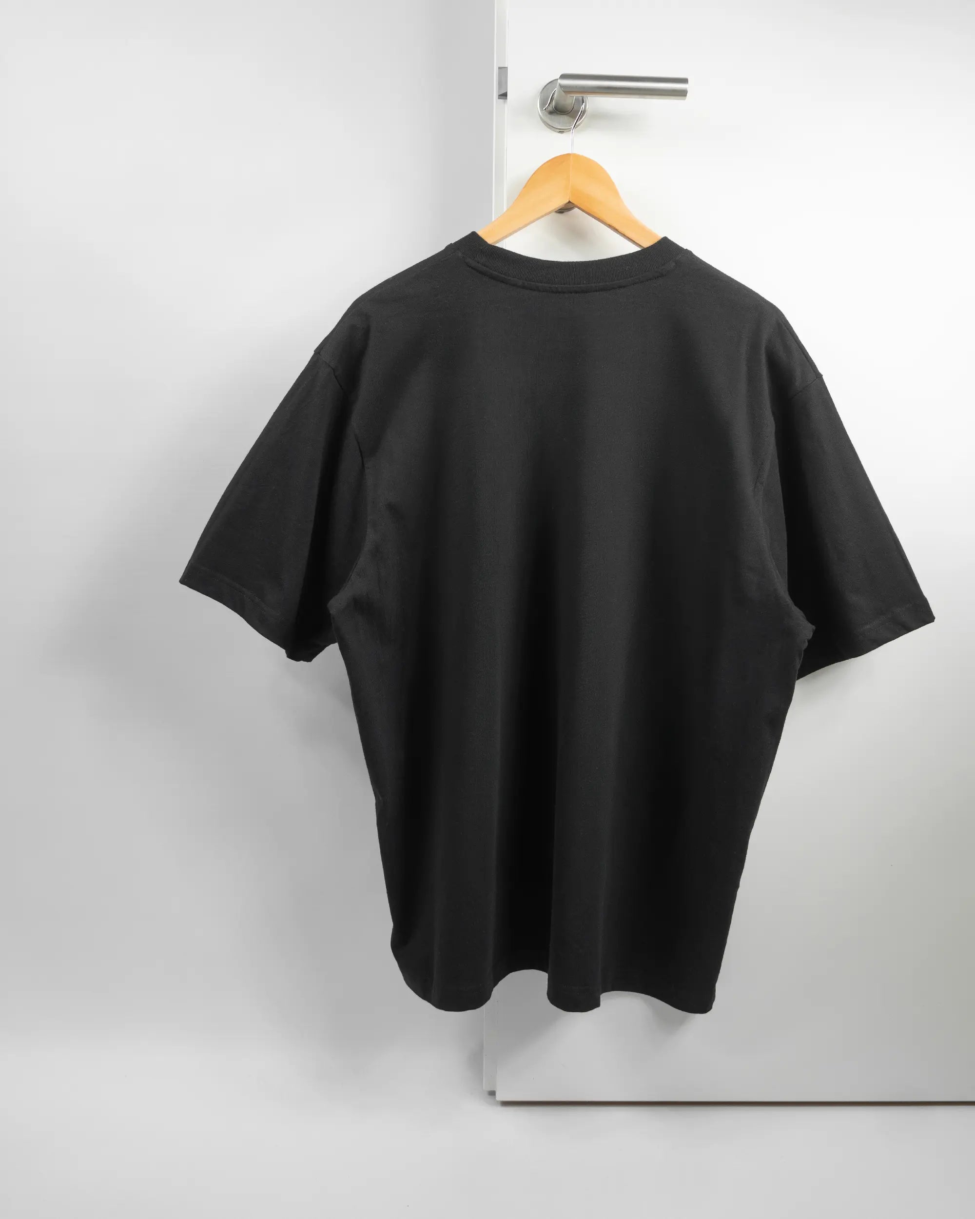 Rückseite des Basic Unisex T-Shirt Oversized von Maondo ohne Motiv in der Farbe Black und in der Größe L auf einem Bügel an der Türklinke aufgehängt