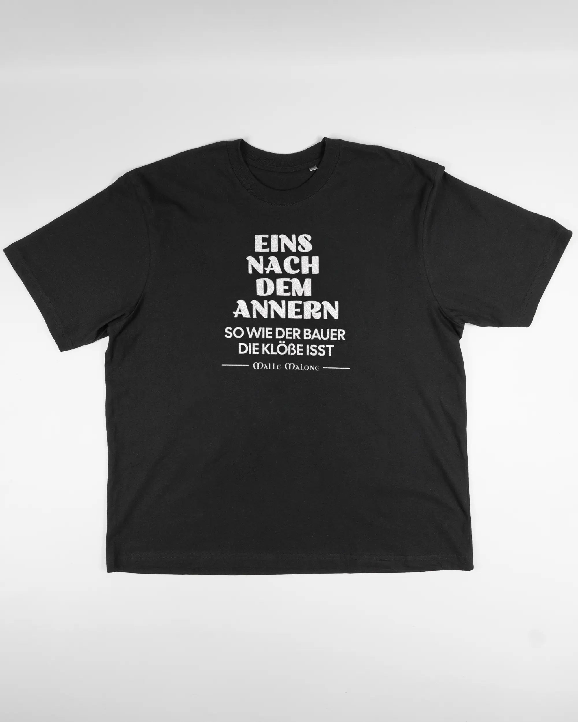 Vorderseite des Basic Unisex T-Shirt Oversized von Maondo mit dem Design Eins nach dem Annern in der Farbe Black und in der Größe L flach auf den Boden gelegt