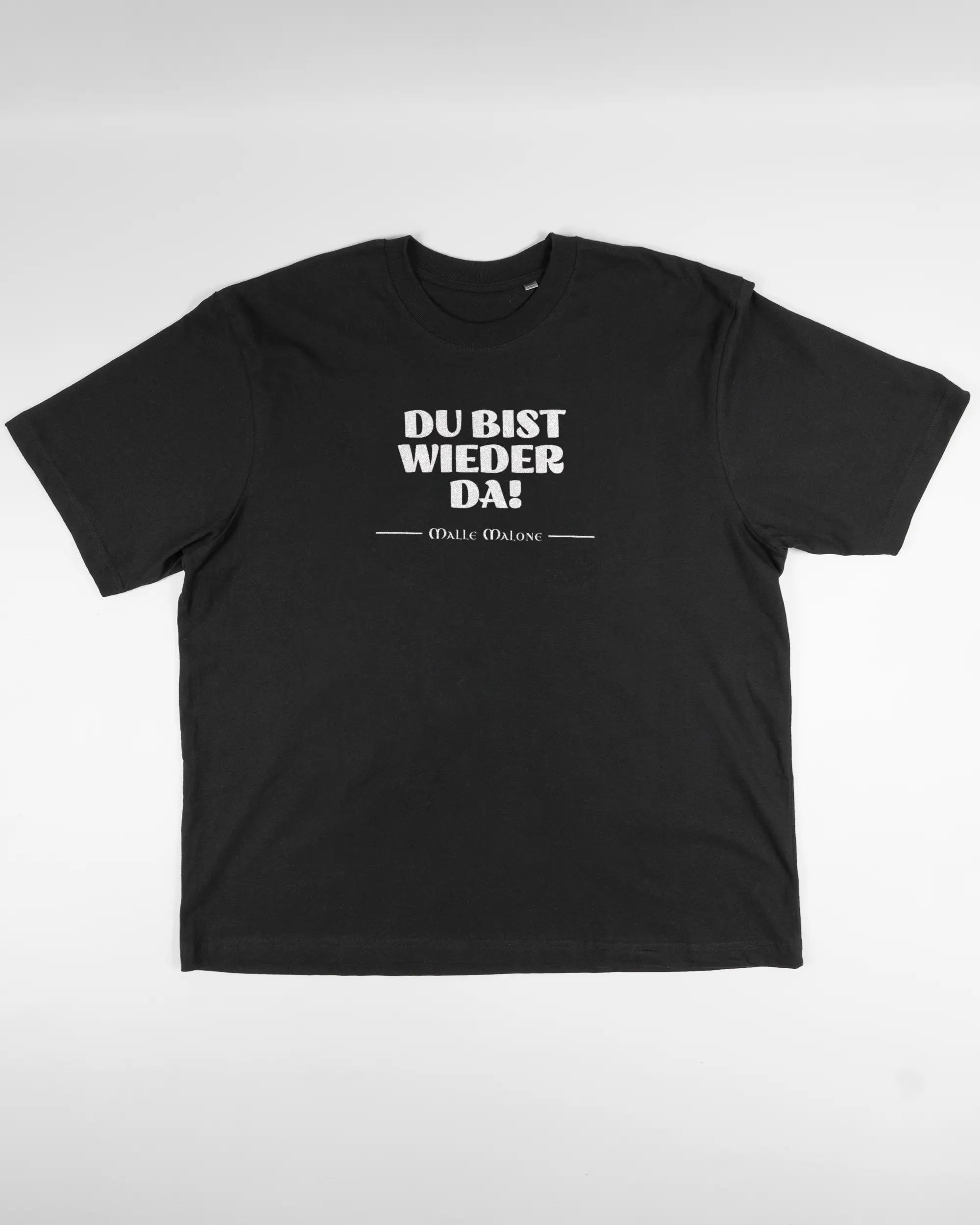 Vorderseite des Basic Unisex T-Shirt Oversized von Maondo mit dem Design Wieder da in der Farbe Black und in der Größe L flach auf den Boden gelegt