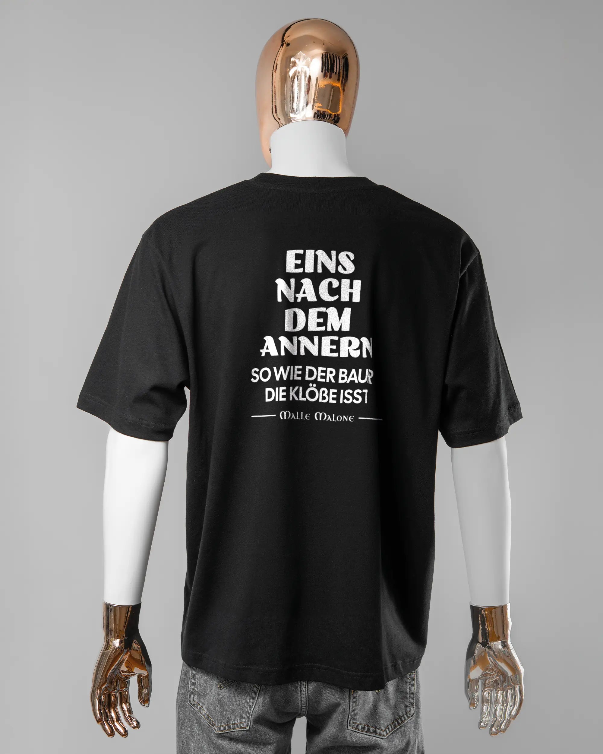 Rückseite des Basic Unisex T-Shirt Oversized von Maondo mit dem Design Eins nach dem Annern in der Farbe Black und in der Größe L getragen von einer maskulinen Puppe