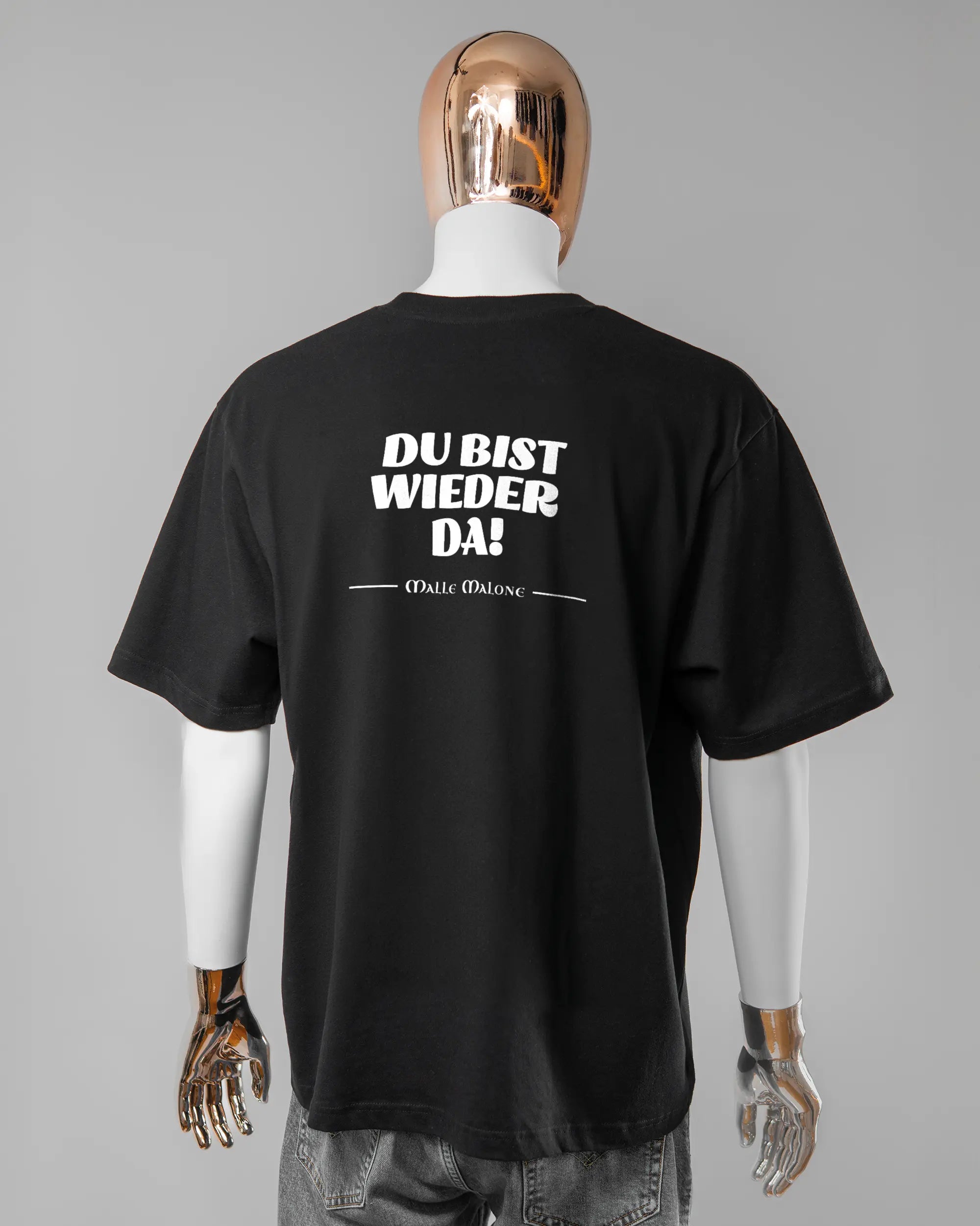 Rückseite des Basic Unisex T-Shirt Oversized von Maondo mit dem Design Wieder da in der Farbe Black und in der Größe L getragen von einer maskulinen Puppe