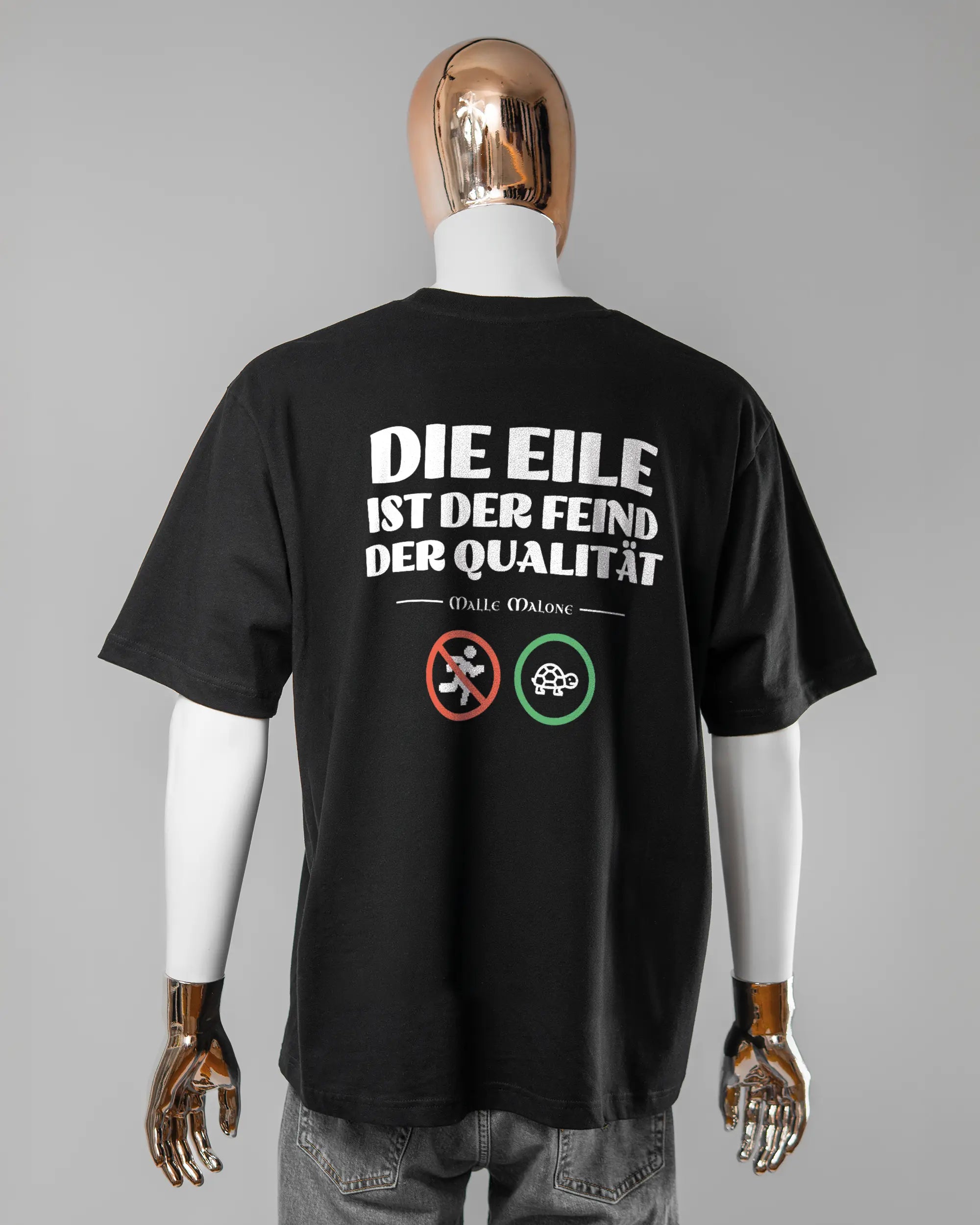 Rückseite des Basic Unisex T-Shirt Oversized von Maondo mit dem Design Keine Eile in der Farbe Black und in der Größe L getragen von einer maskulinen Puppe