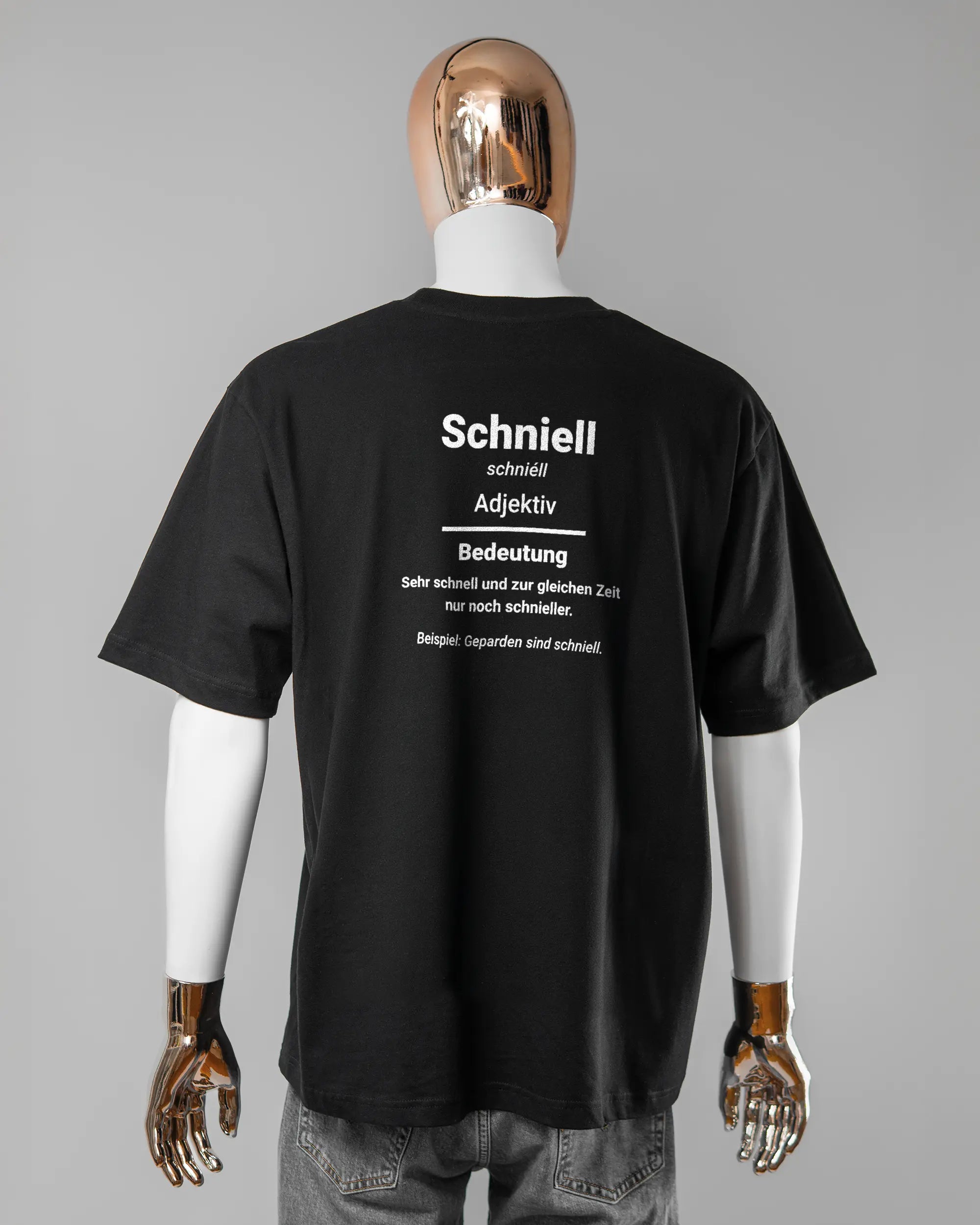 Rückseite des Basic Unisex T-Shirt Oversized von Maondo mit dem Design Schniell in der Farbe Black und in der Größe L getragen von einer maskulinen Puppe