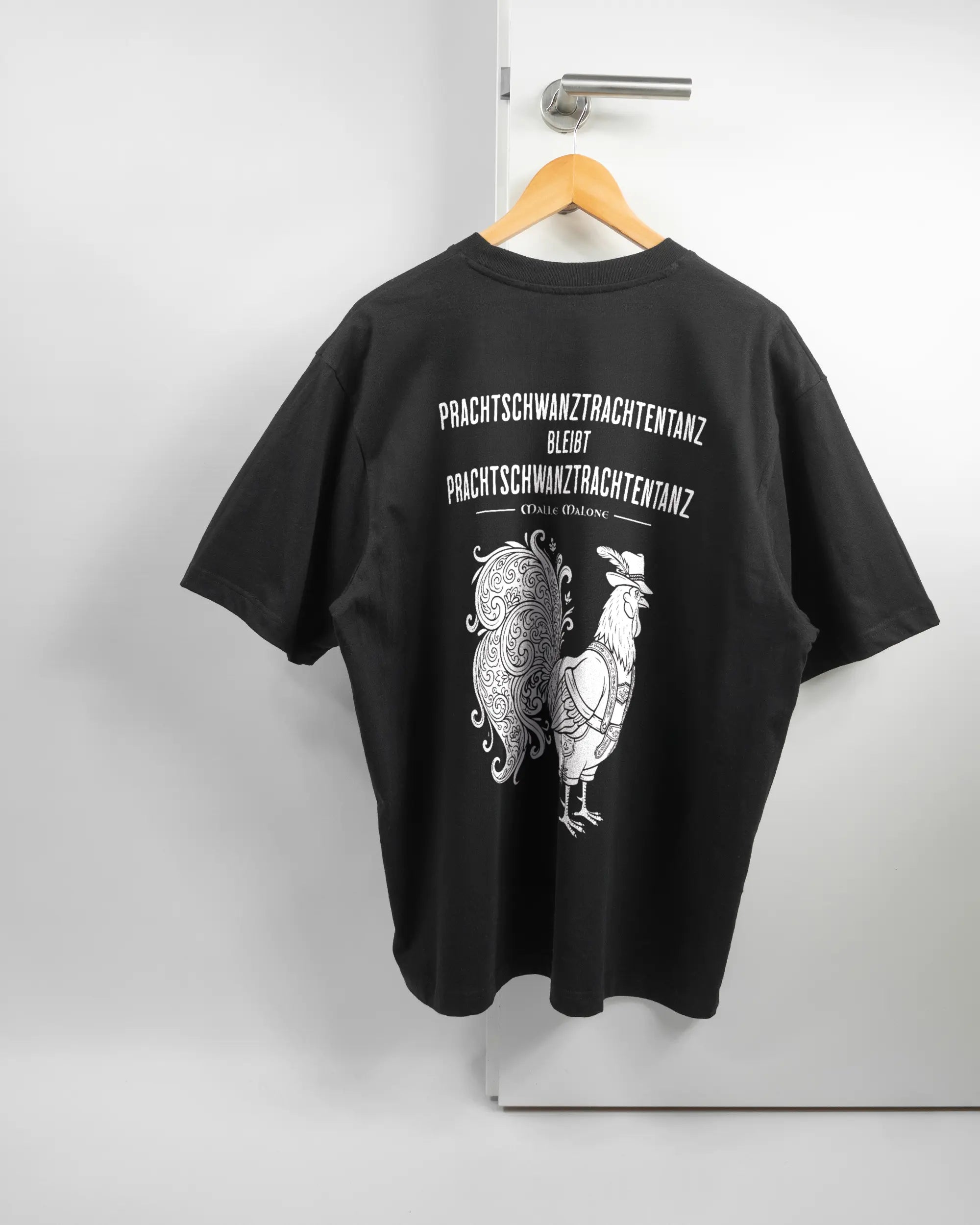 Rückseite des Basic Unisex T-Shirt Oversized von Maondo mit dem Design Trachtentanz in der Farbe Black und in der Größe L auf einem Bügel an der Türklinke aufgehängt