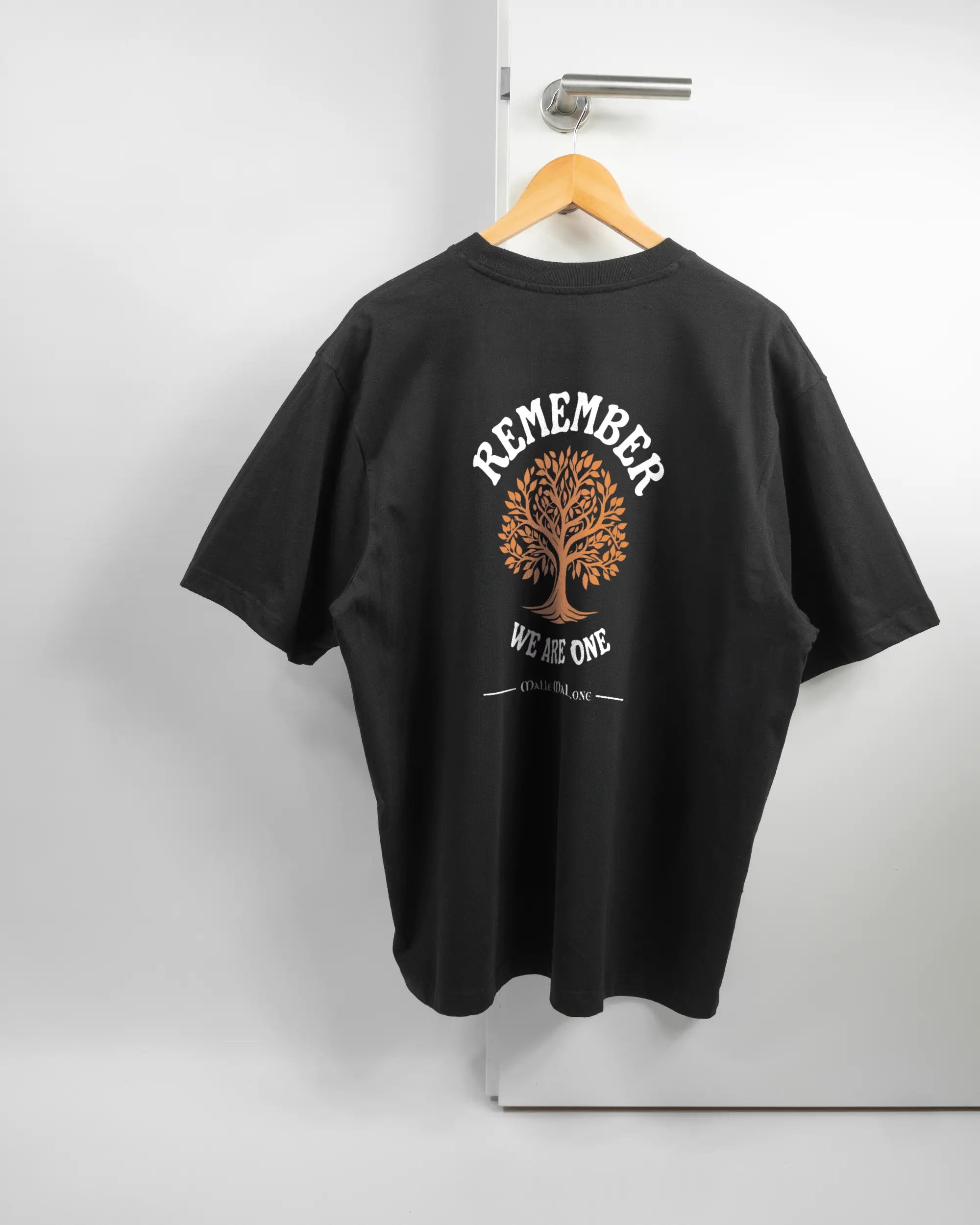 Rückseite des Basic Unisex T-Shirt Oversized von Maondo mit dem Design We are one in der Farbe Black und in der Größe L auf einem Bügel an der Türklinke aufgehängt