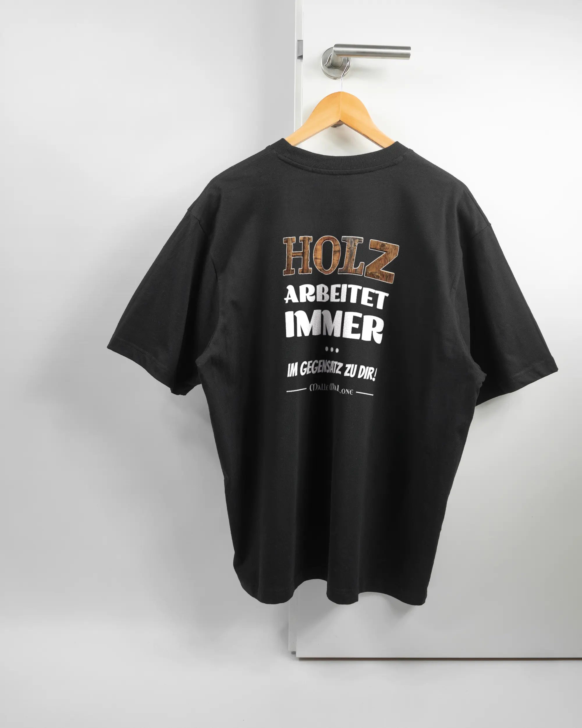 Rückseite des Basic Unisex T-Shirt Oversized von Maondo mit dem Design Holzarbeit in der Farbe Black und in der Größe L auf einem Bügel an der Türklinke aufgehängt