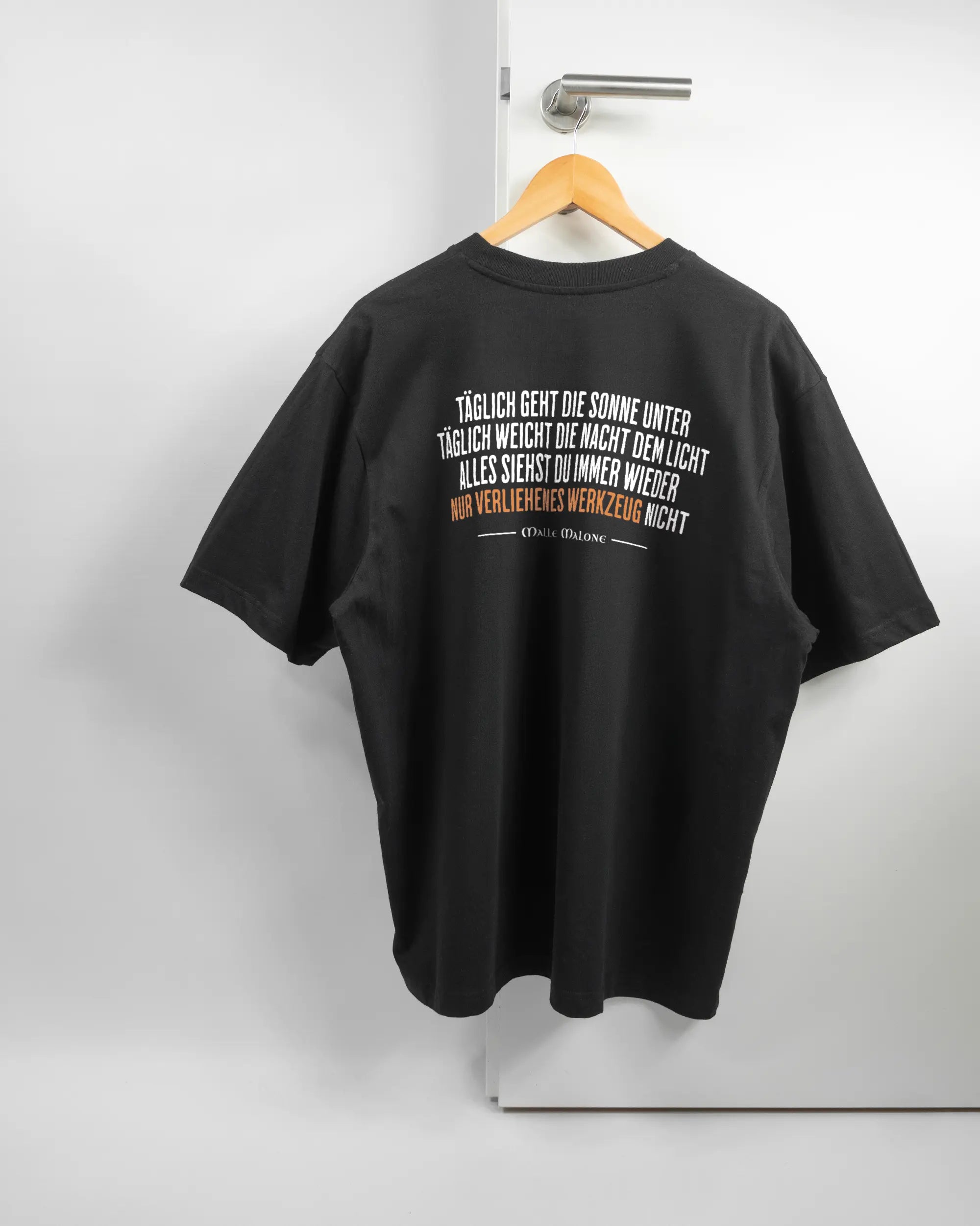 Rückseite des Basic Unisex T-Shirt Oversized von Maondo mit dem Design Wegzeug in der Farbe Black und in der Größe L auf einem Bügel an der Türklinke aufgehängt