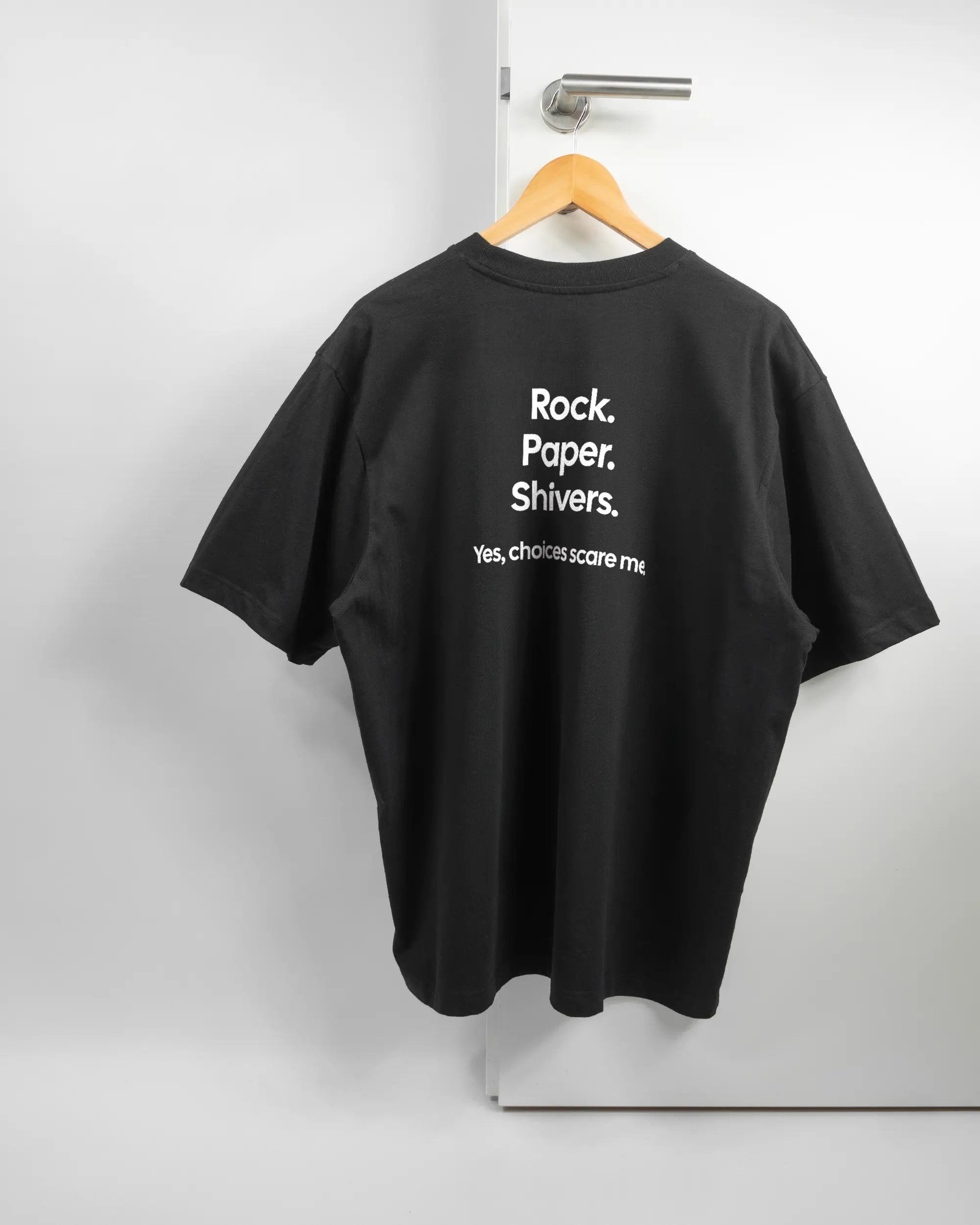 Rückseite des Basic Unisex T-Shirt Oversized von Maondo mit dem Design Rock Paper Shivers in der Farbe Black und in der Größe L auf einem Bügel an der Türklinke aufgehängt