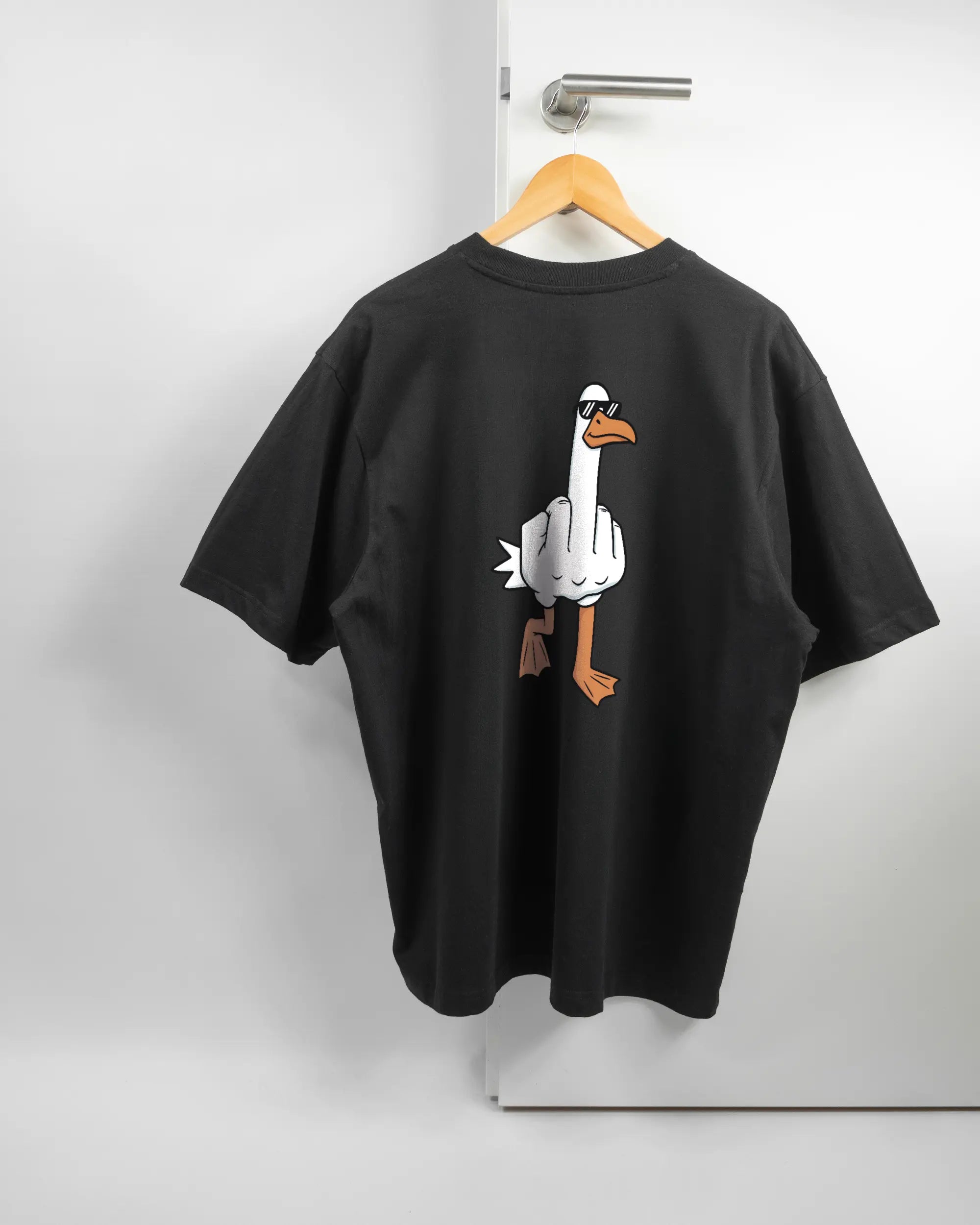 Rückseite des Basic Unisex T-Shirt Oversized von Maondo mit dem Design I give a duck in der Farbe Black und in der Größe L auf einem Bügel an der Türklinke aufgehängt