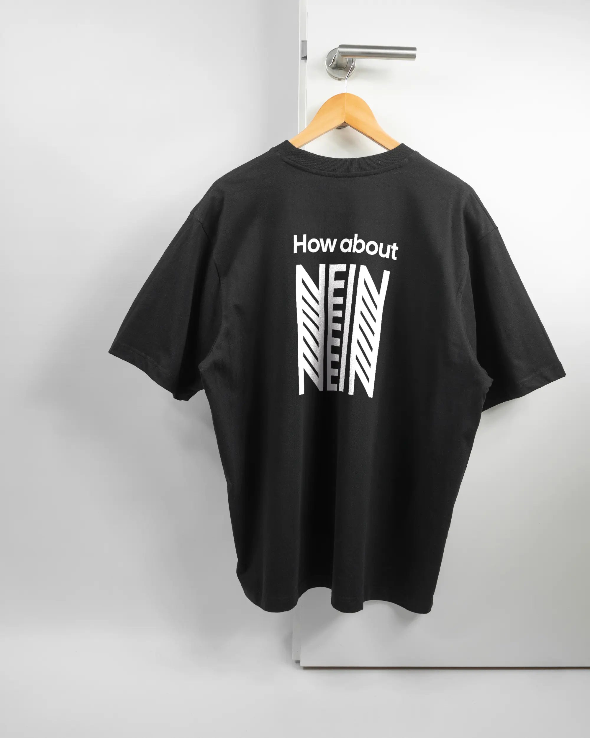 Rückseite des Basic Unisex T-Shirt Oversized von Maondo mit dem Design How about nein in der Farbe Black und in der Größe L auf einem Bügel an der Türklinke aufgehängt