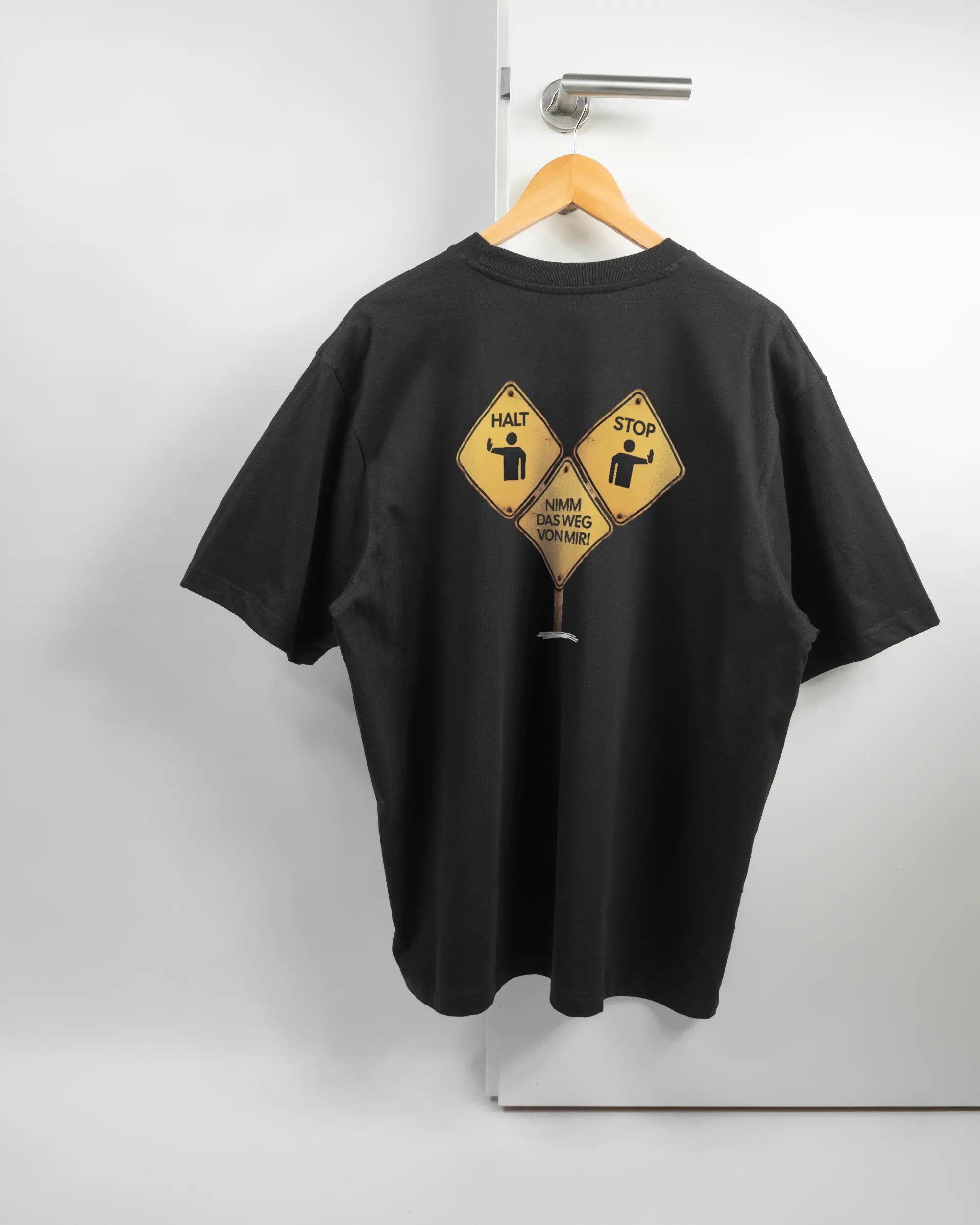 Rückseite des Basic Unisex T-Shirt Oversized von Maondo mit dem Design Schutzschild in der Farbe Black und in der Größe L auf einem Bügel an der Türklinke aufgehängt
