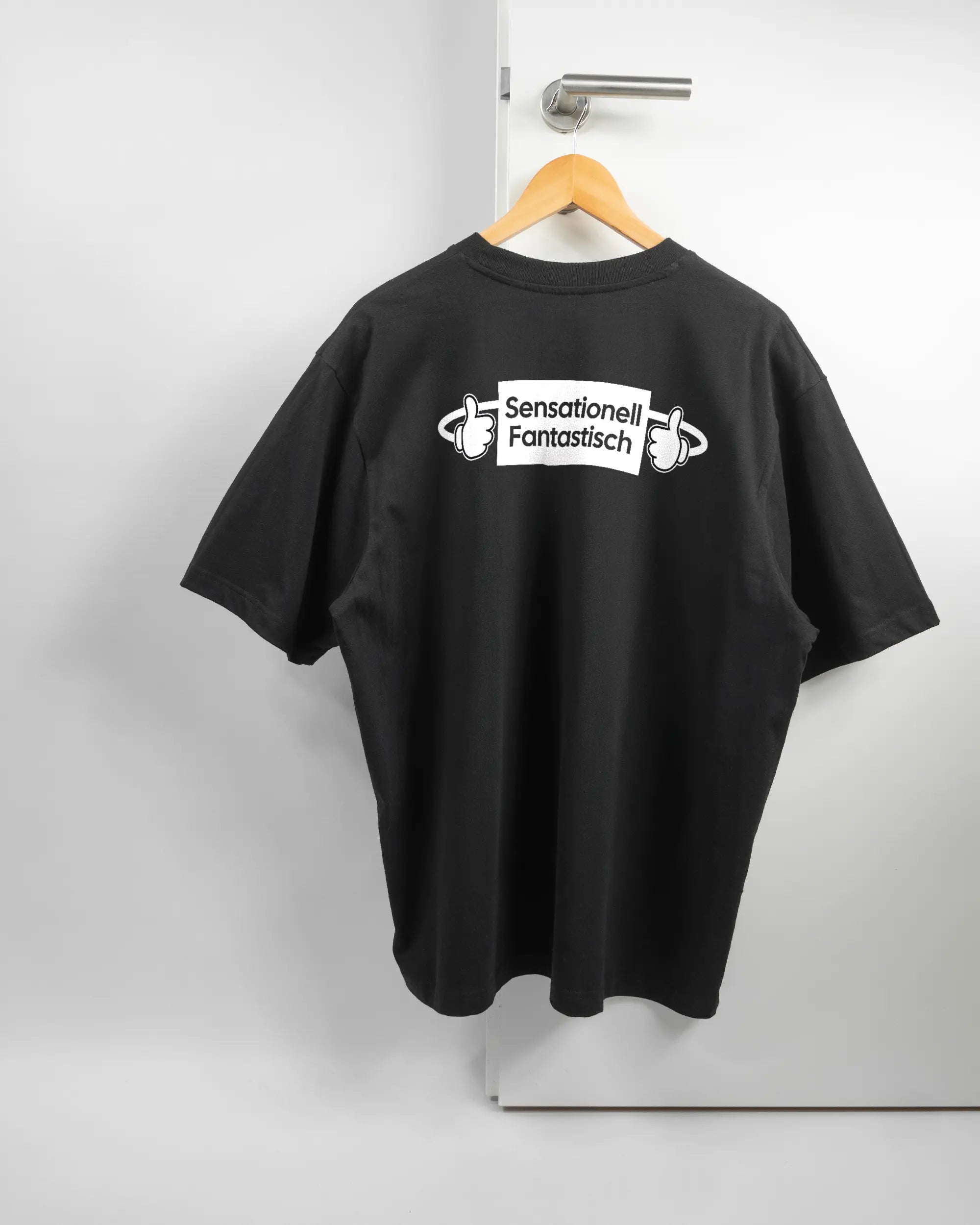 Rückseite des Basic Unisex T-Shirt Oversized von Maondo mit dem Design Fantastisch in der Farbe Black und in der Größe L auf einem Bügel an der Türklinke aufgehängt