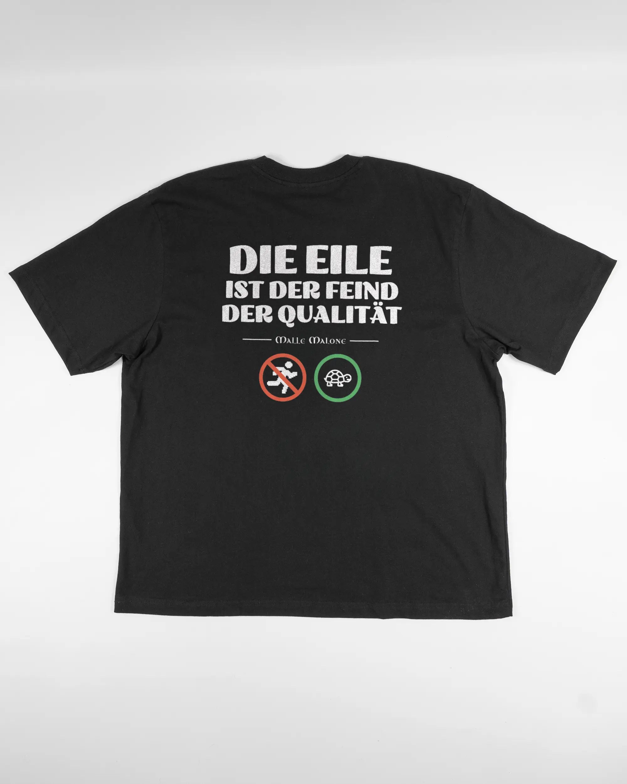 Rückseite des Basic Unisex T-Shirt Oversized von Maondo mit dem Design Keine Eile in der Farbe Black und in der Größe L flach auf den Boden gelegt