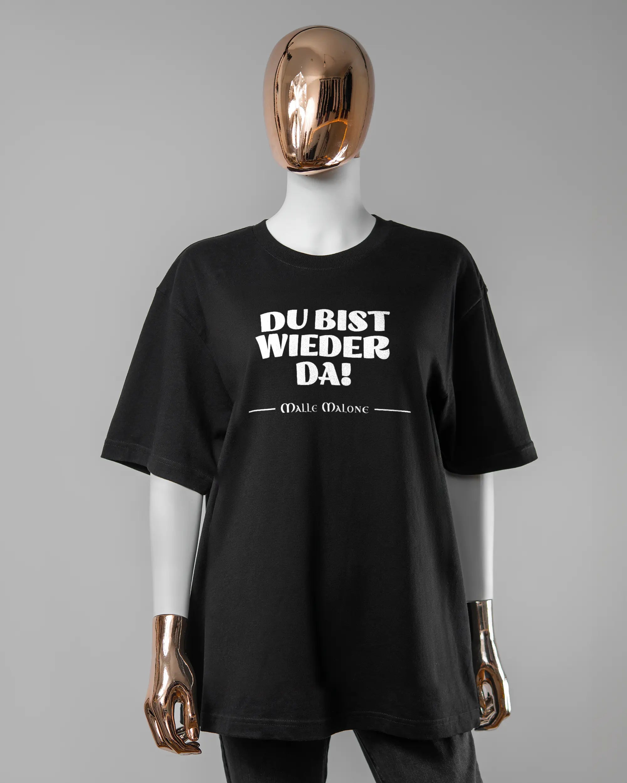 Vorderseite des Basic Unisex T-Shirt Oversized von Maondo mit dem Design Wieder da in der Farbe Black und in der Größe S getragen von einer femininen Puppe