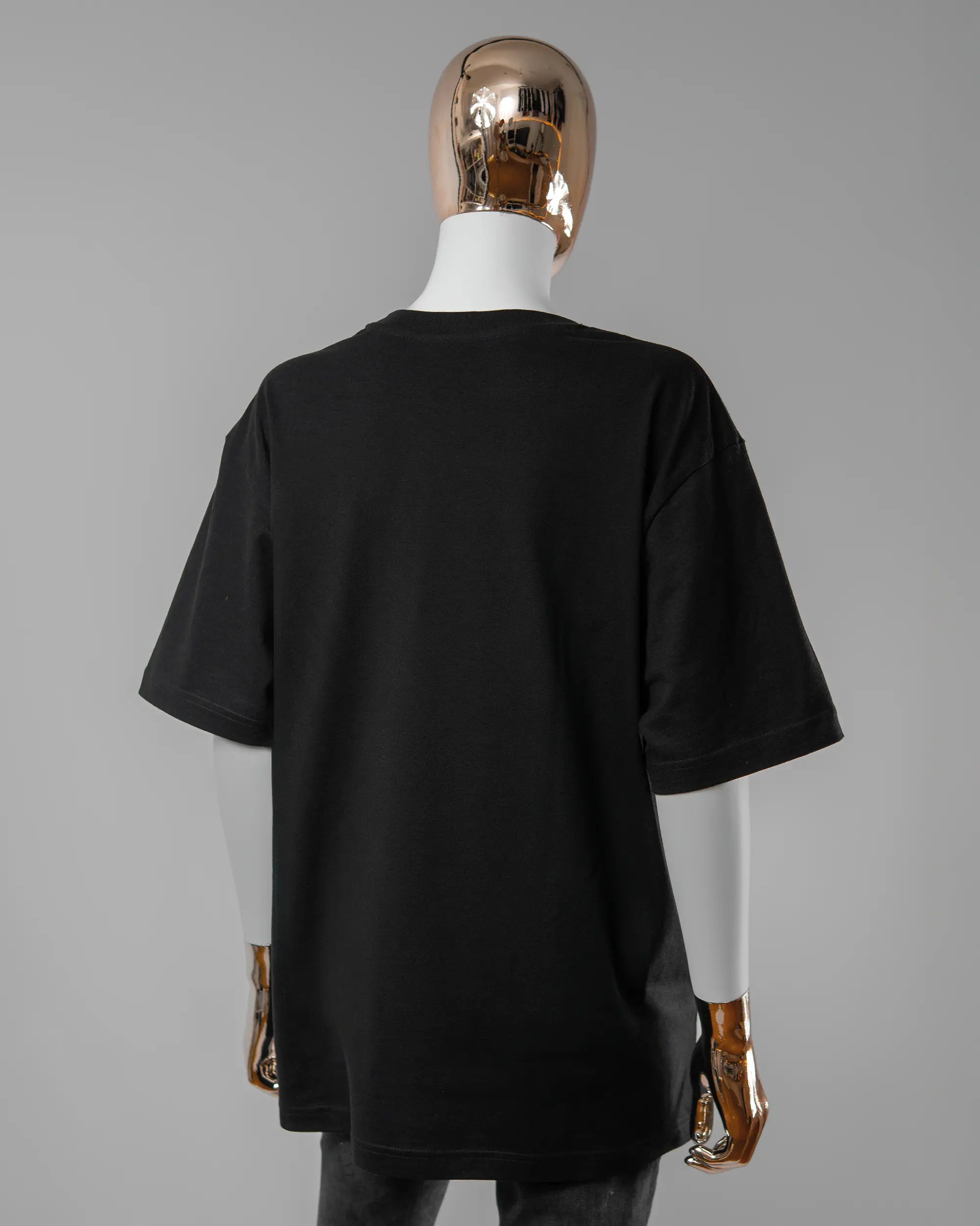 Rückseite des Basic Unisex T-Shirt Oversized von Maondo ohne Motiv in der Farbe Black und in der Größe S getragen von einer femininen Puppe