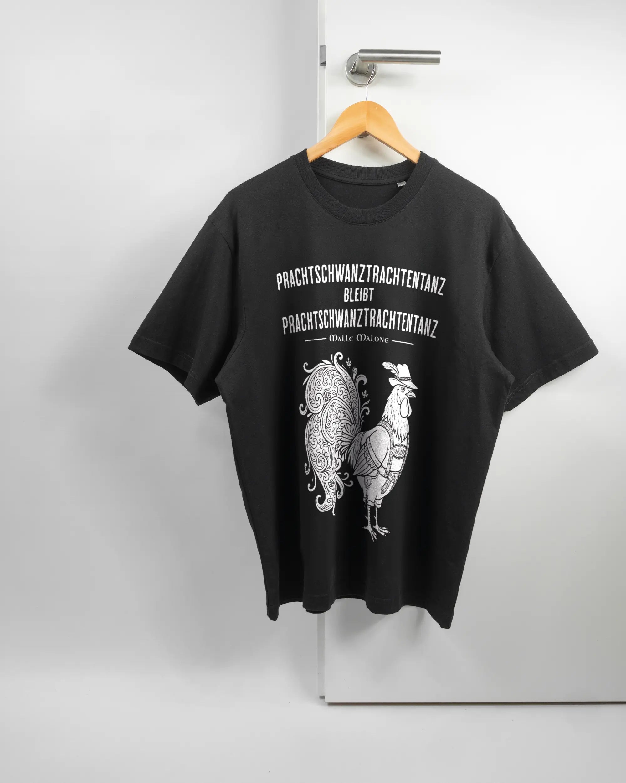 Vorderseite des Basic Unisex T-Shirt Oversized von Maondo mit dem Design Trachtentanz in der Farbe Black und in der Größe S auf einem Bügel an der Türklinke aufgehängt