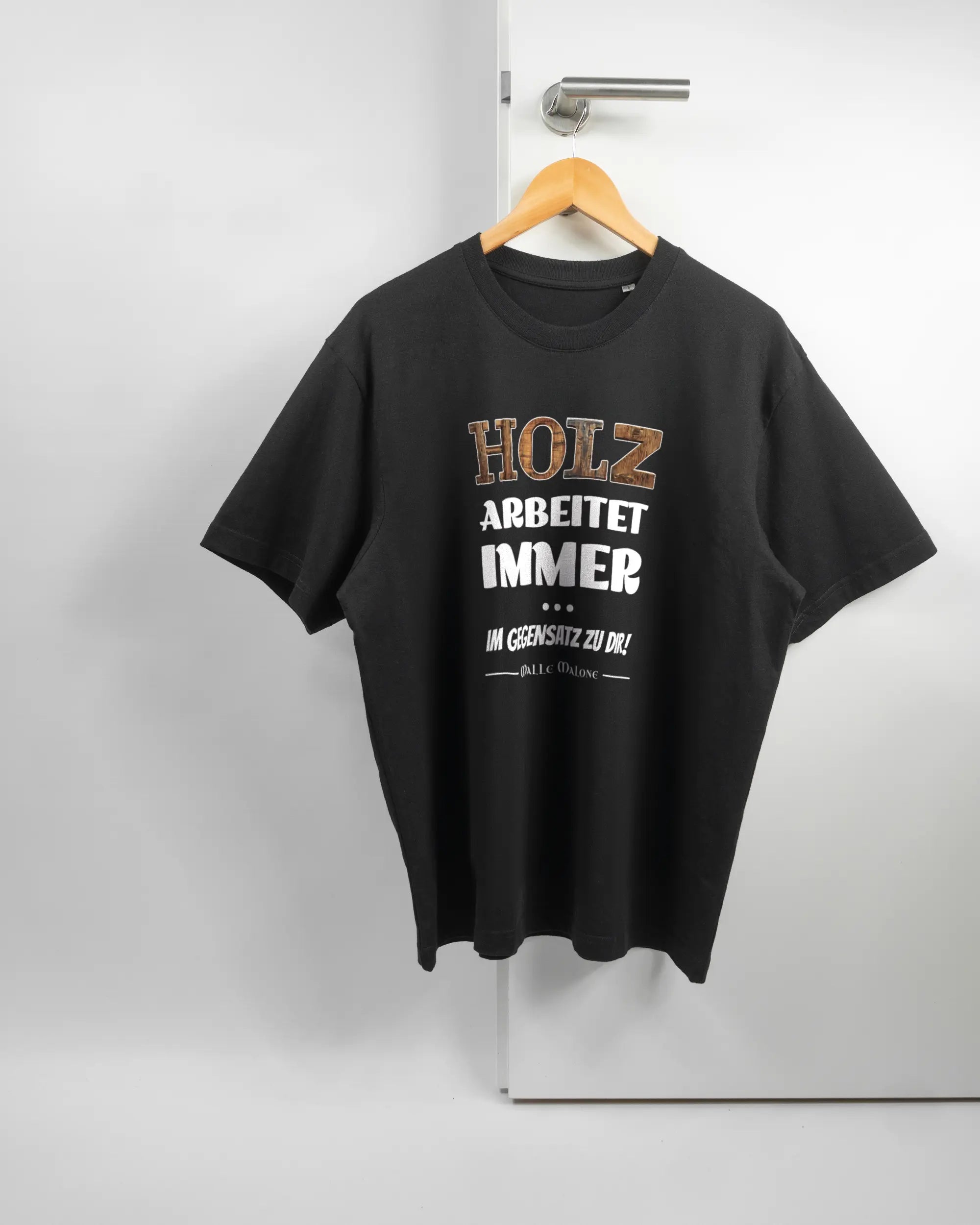 Vorderseite des Basic Unisex T-Shirt Oversized von Maondo mit dem Design Holzarbeit in der Farbe Black und in der Größe S auf einem Bügel an der Türklinke aufgehängt