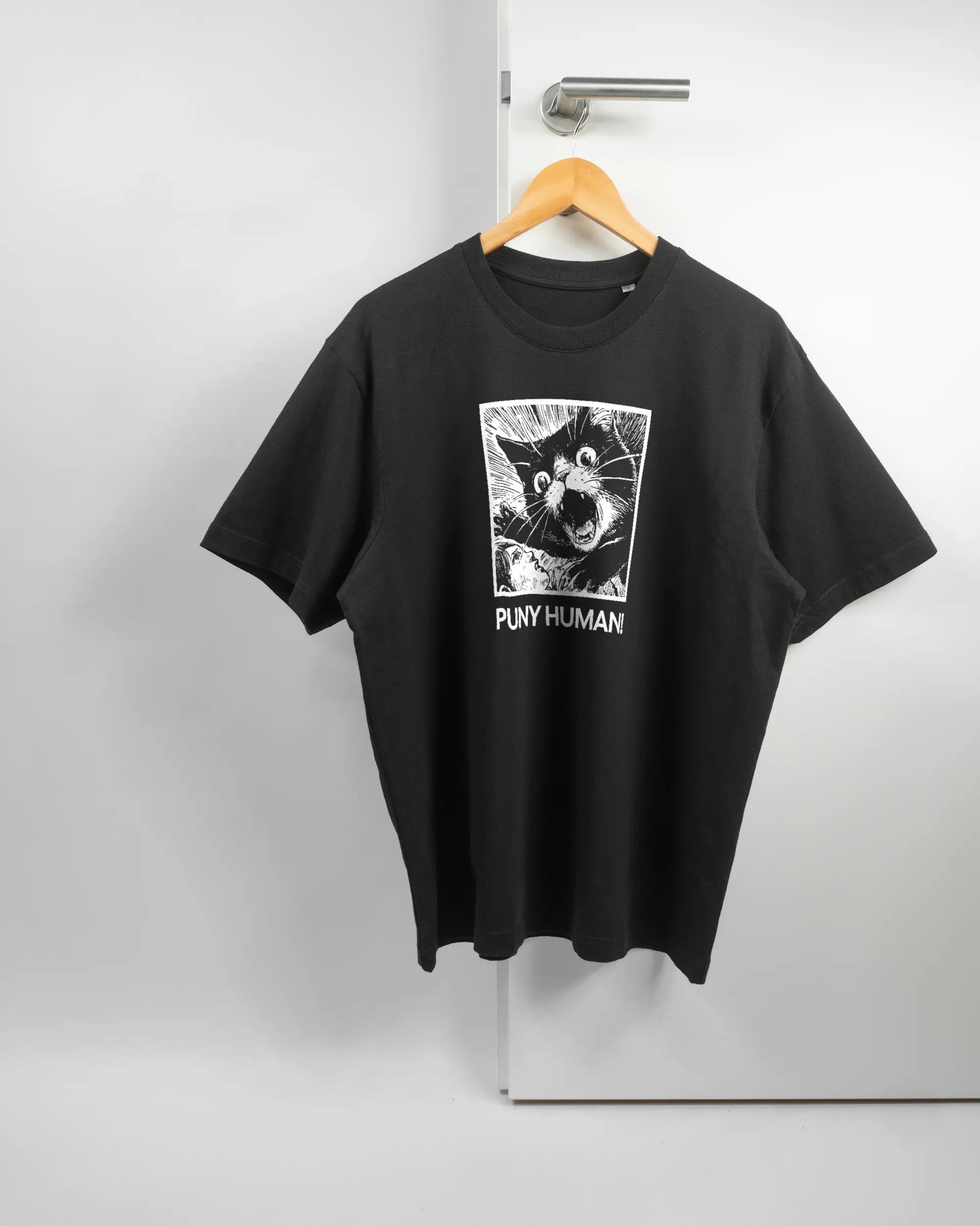 Vorderseite des Basic Unisex T-Shirt Oversized von Maondo mit dem Design Puny Human in der Farbe Black und in der Größe S auf einem Bügel an der Türklinke aufgehängt