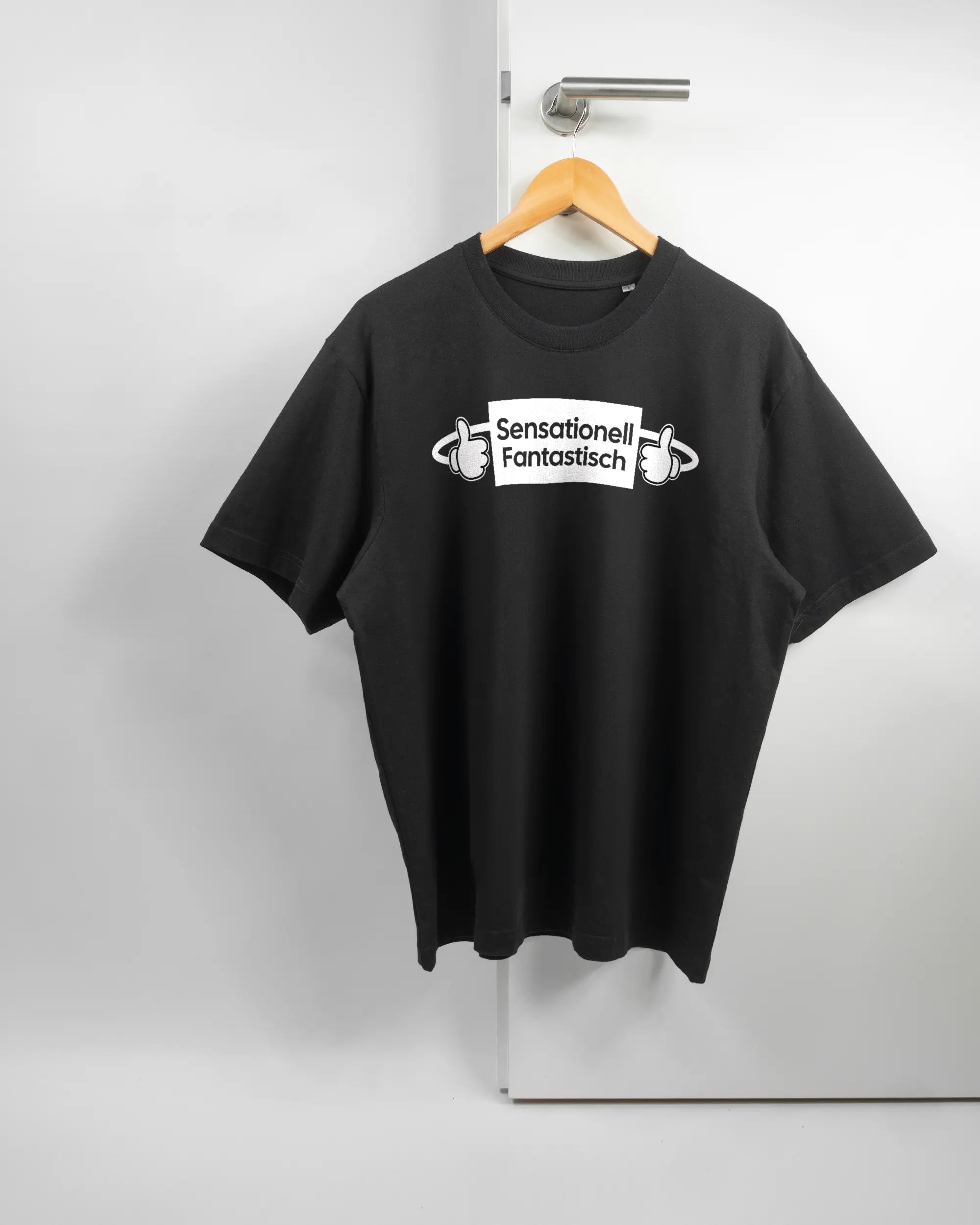 Vorderseite des Basic Unisex T-Shirt Oversized von Maondo mit dem Design Fantastisch in der Farbe Black und in der Größe S auf einem Bügel an der Türklinke aufgehängt