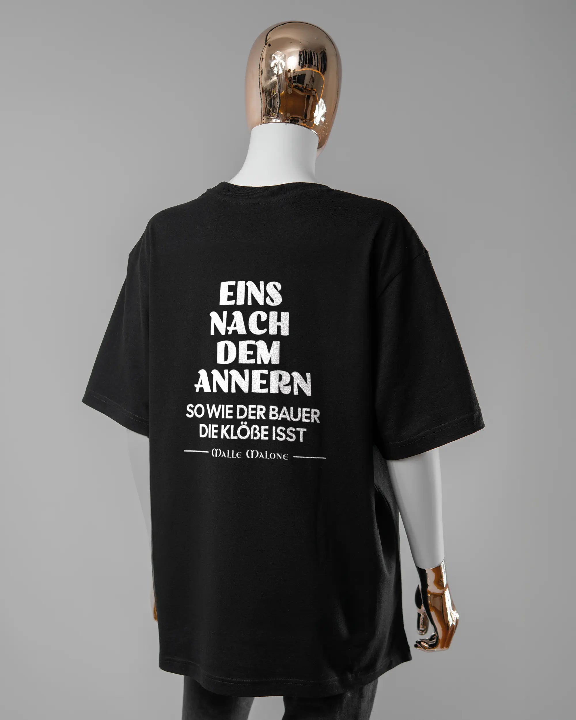 Rückseite des Basic Unisex T-Shirt Oversized von Maondo mit dem Design Eins nach dem Annern in der Farbe Black und in der Größe S getragen von einer femininen Puppe