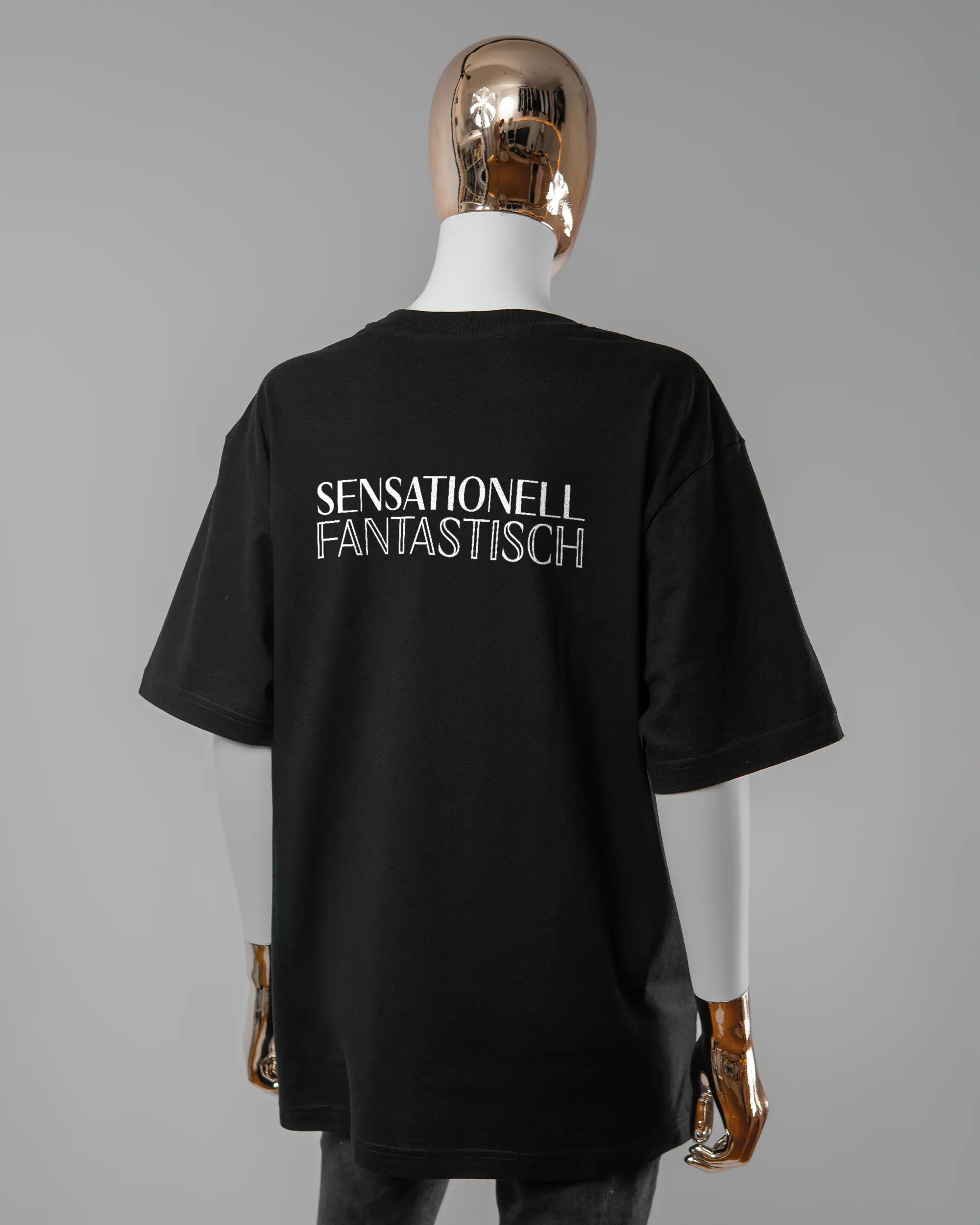 Rückseite des Basic Unisex T-Shirt Oversized von Maondo mit dem Design Sensationell in der Farbe Black und in der Größe S getragen von einer femininen Puppe