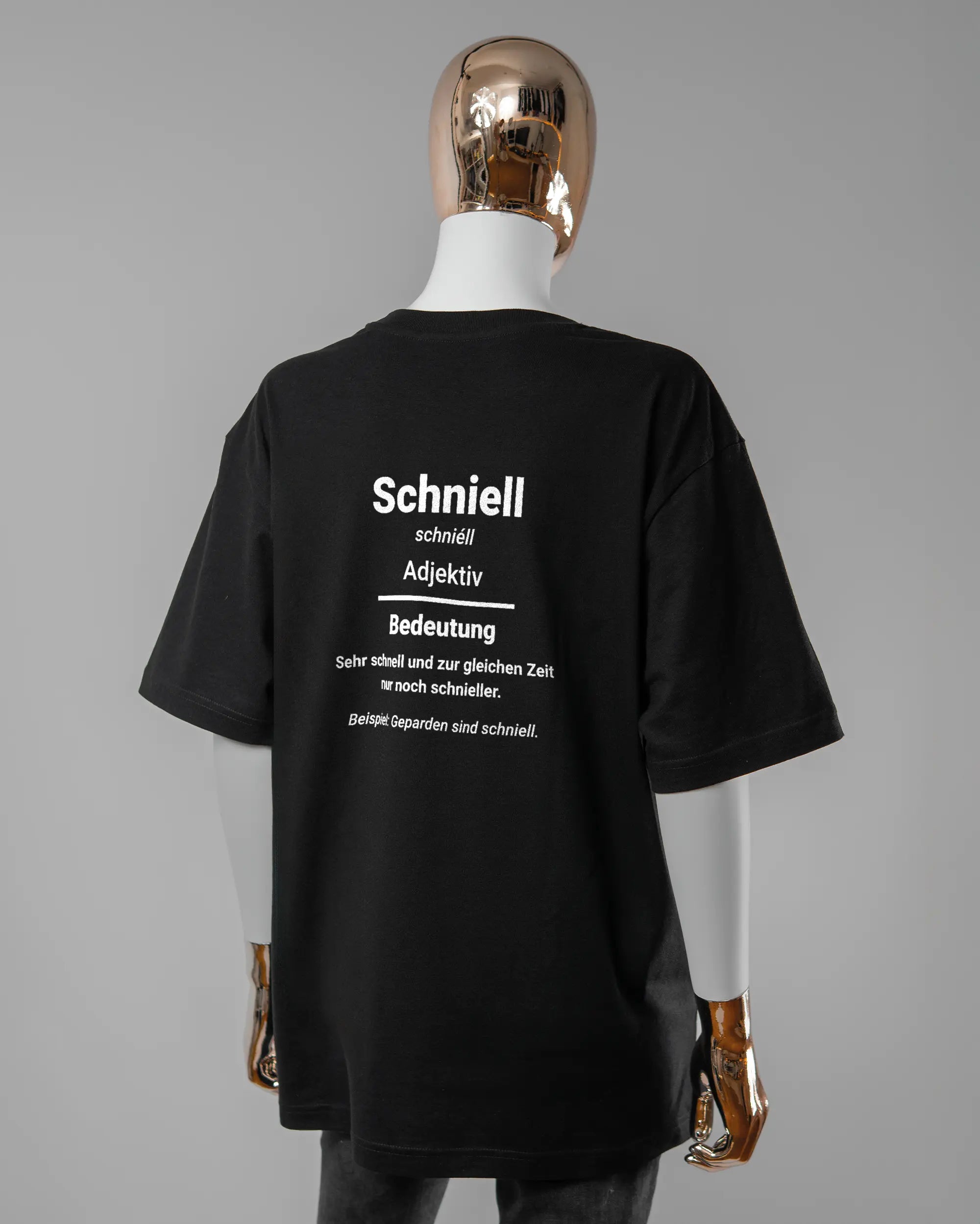 Rückseite des Basic Unisex T-Shirt Oversized von Maondo mit dem Design Schniell in der Farbe Black und in der Größe S getragen von einer femininen Puppe