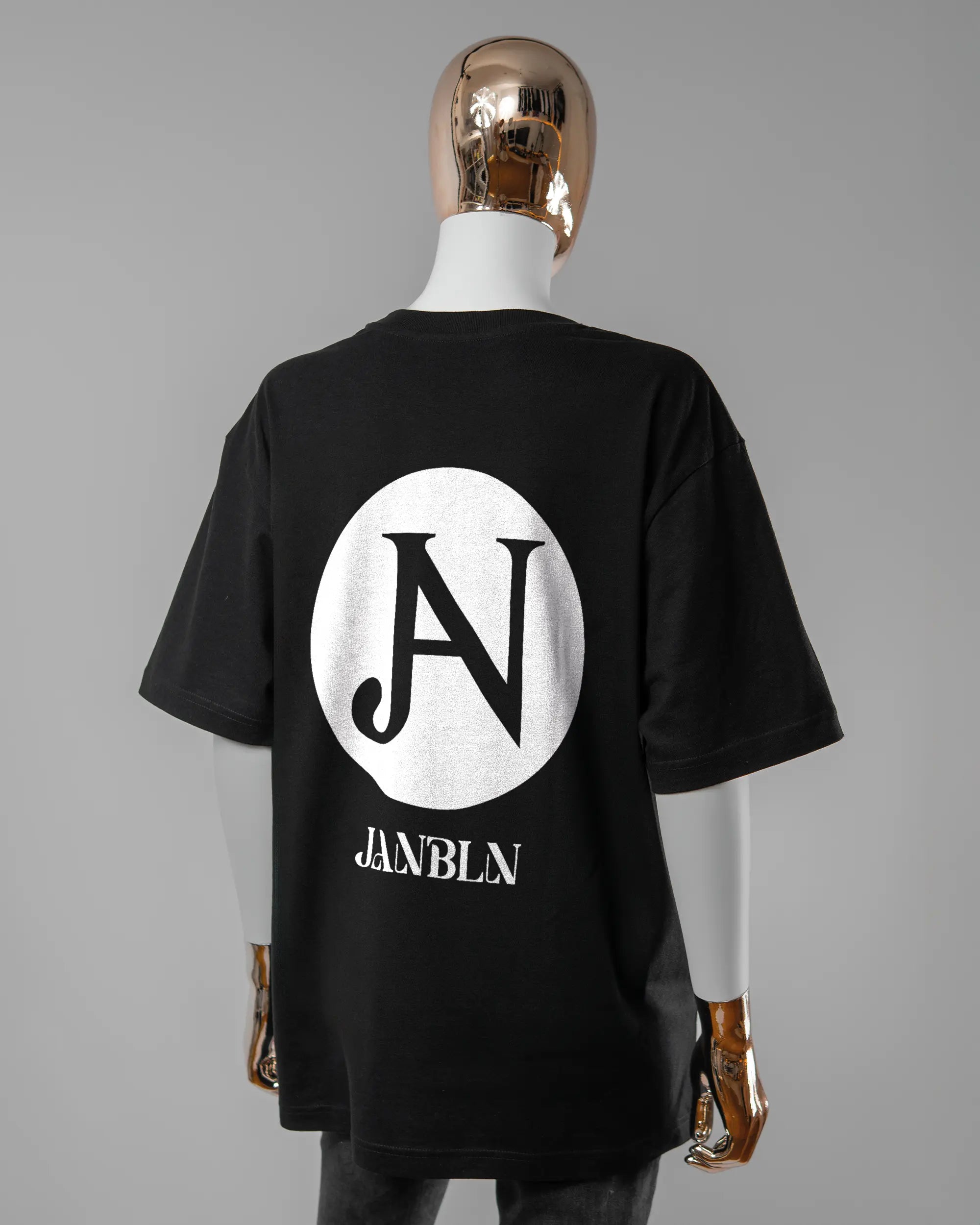 Rückseite des Basic Unisex T-Shirt Oversized von Maondo mit dem Design JB1 in der Farbe Black und in der Größe S getragen von einer femininen Puppe