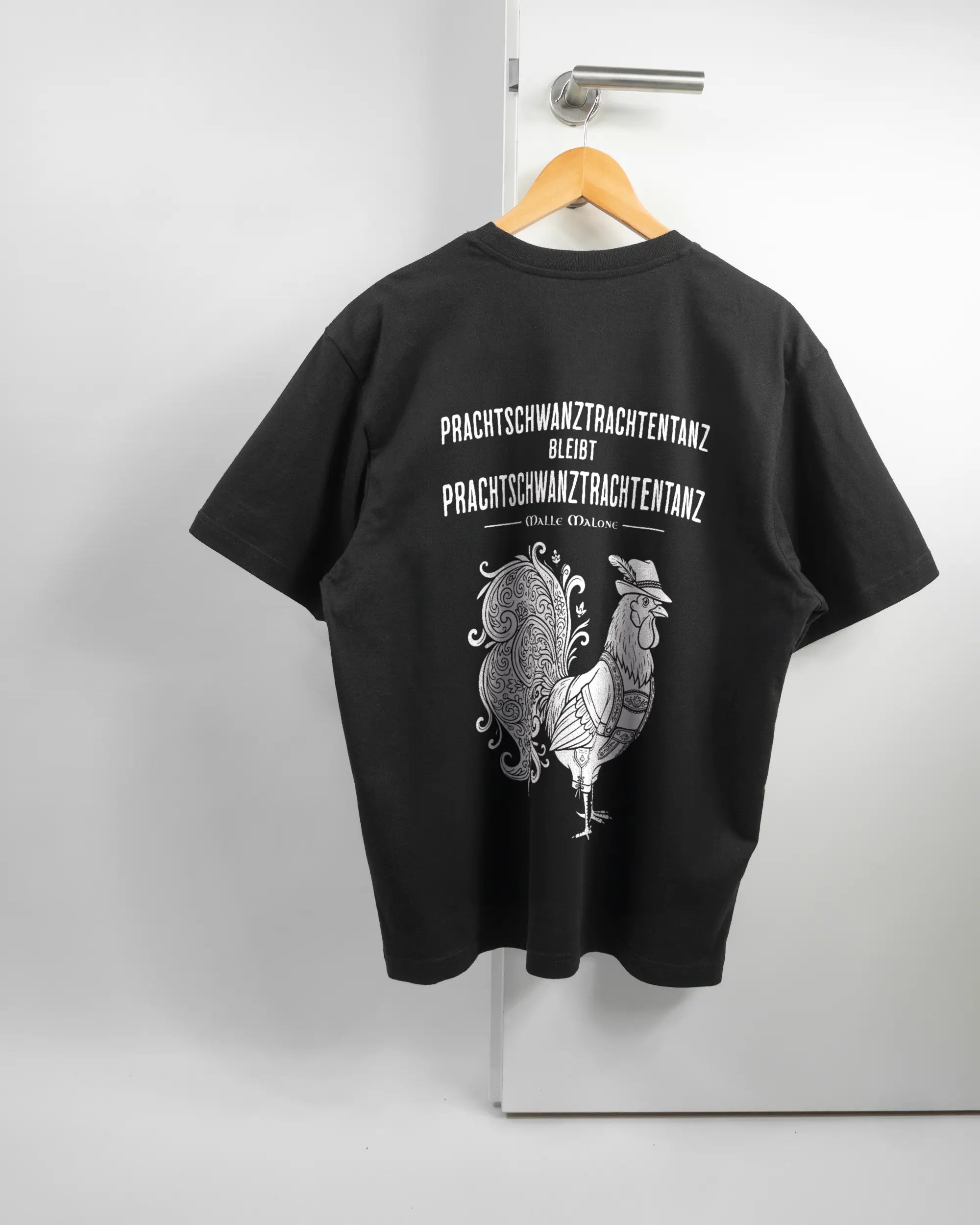 Rückseite des Basic Unisex T-Shirt Oversized von Maondo mit dem Design Trachtentanz in der Farbe Black und in der Größe S auf einem Bügel an der Türklinke aufgehängt