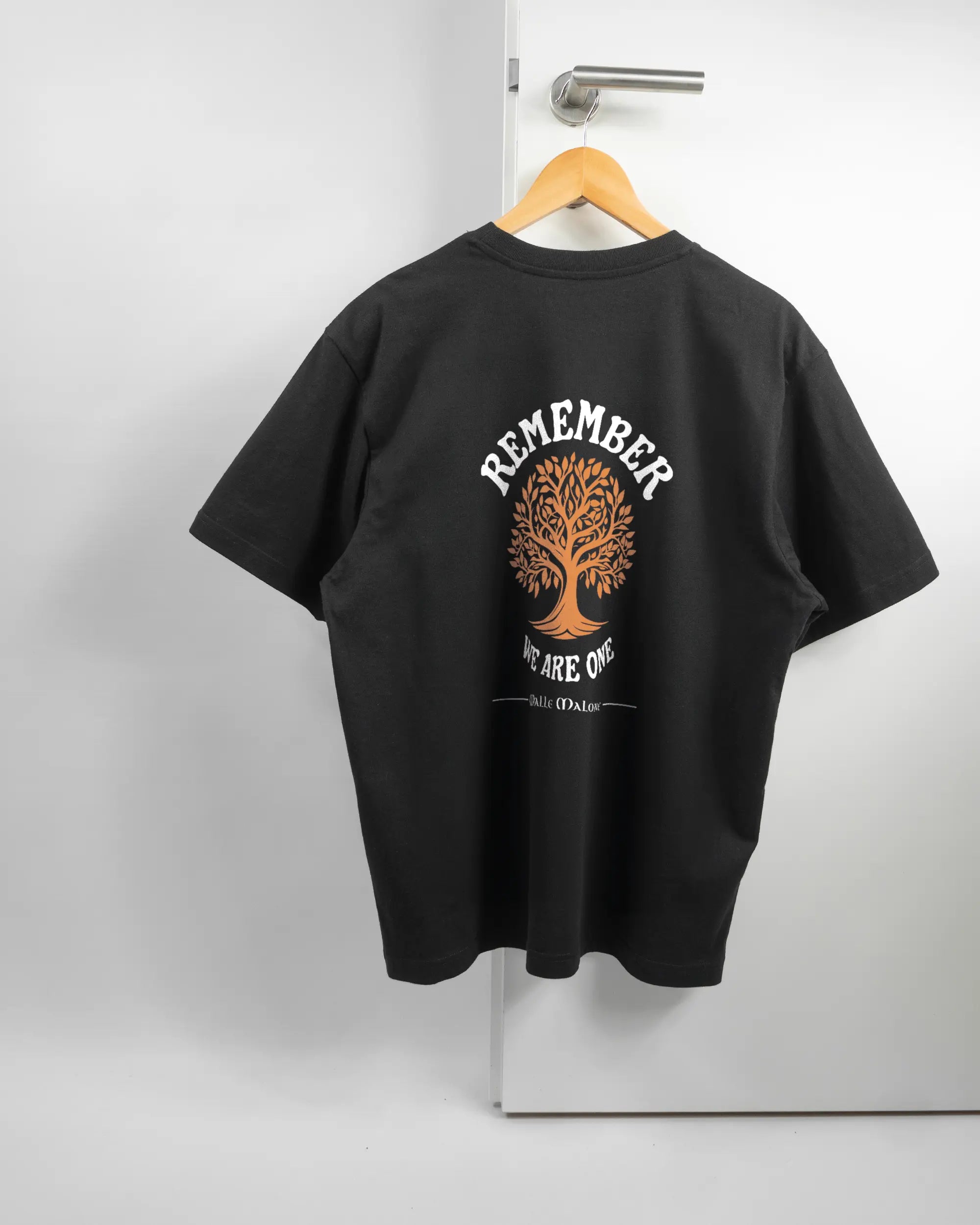 Rückseite des Basic Unisex T-Shirt Oversized von Maondo mit dem Design We are one in der Farbe Black und in der Größe S auf einem Bügel an der Türklinke aufgehängt