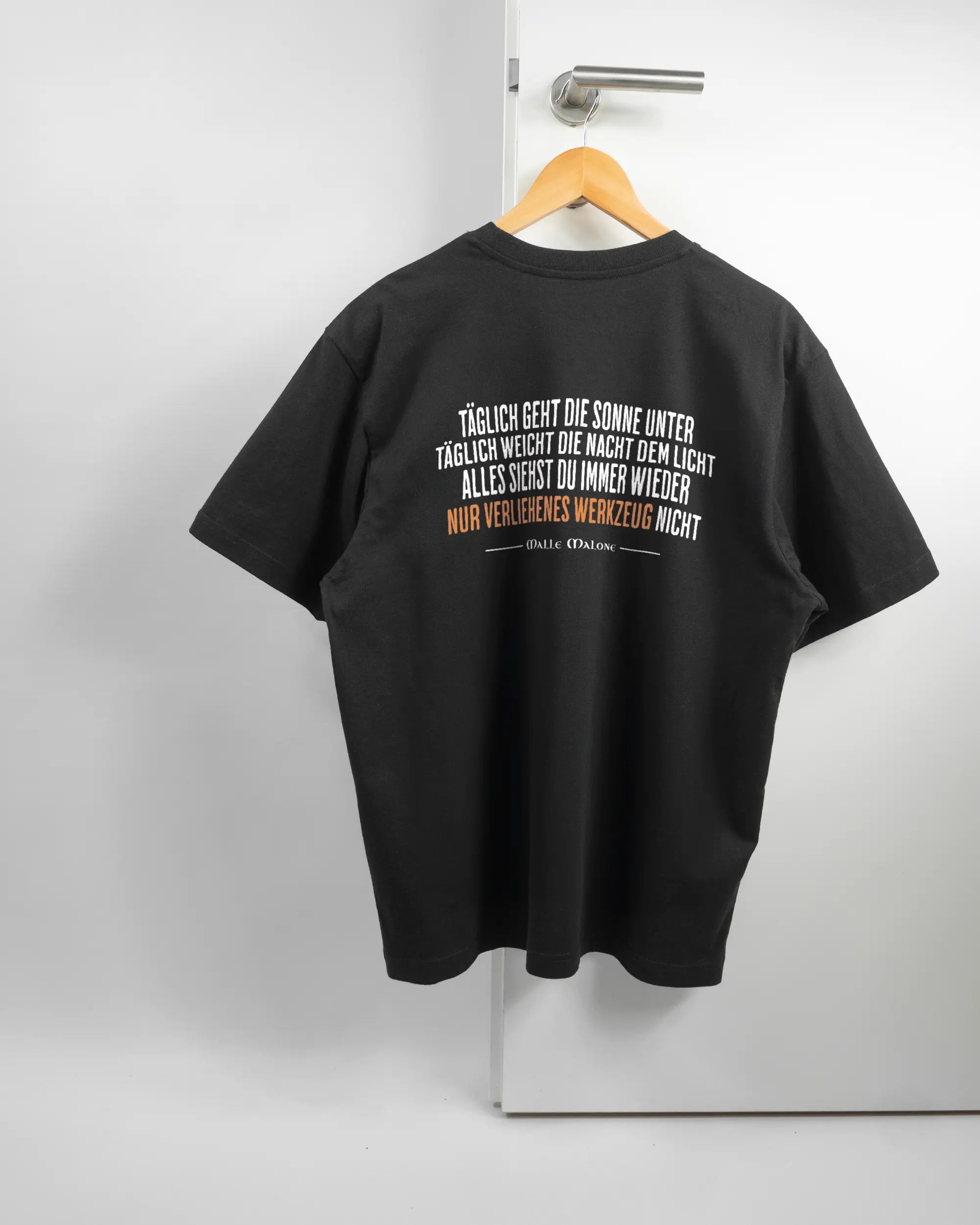 Rückseite des Basic Unisex T-Shirt Oversized von Maondo mit dem Design Wegzeug in der Farbe Black und in der Größe S auf einem Bügel an der Türklinke aufgehängt