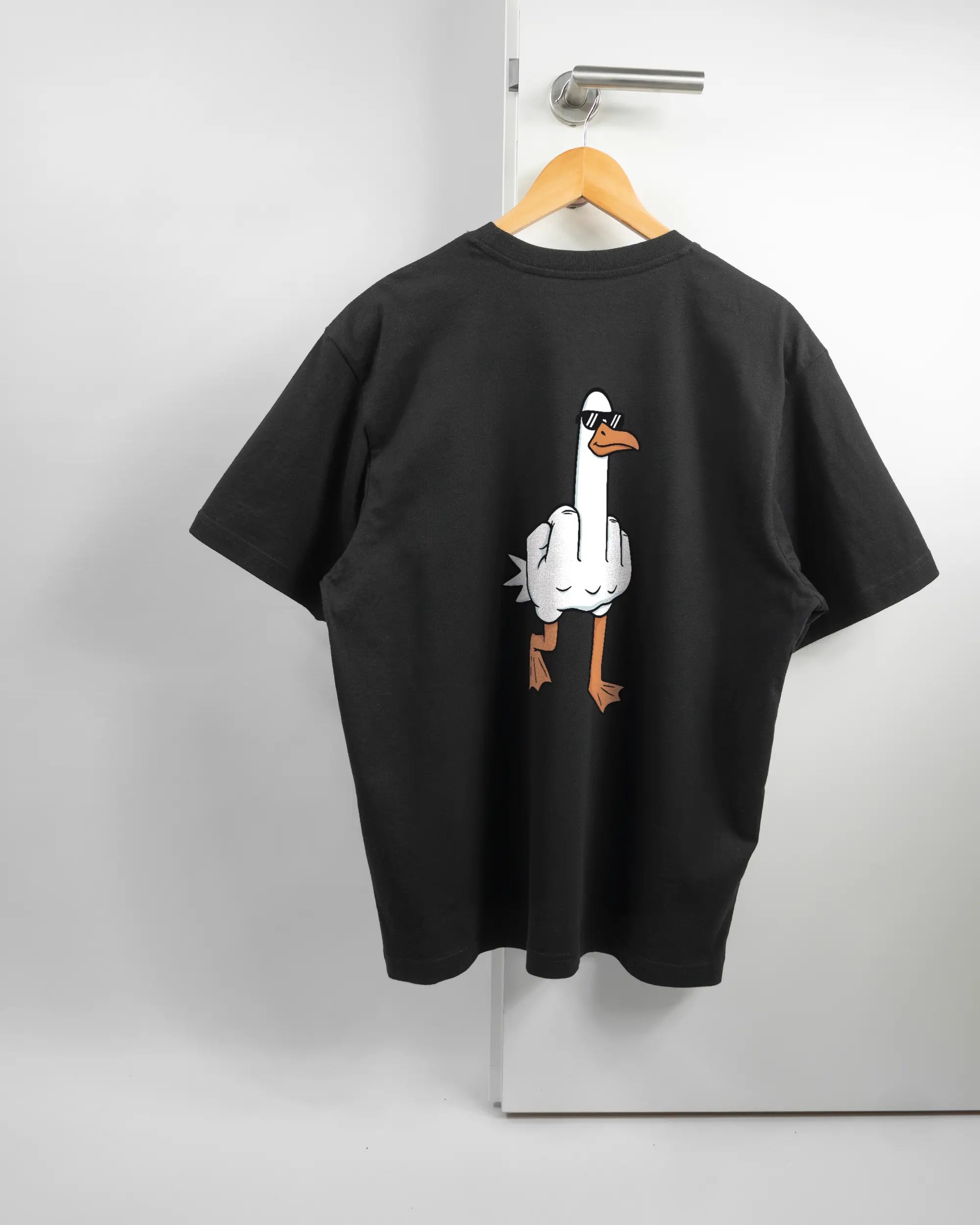 Rückseite des Basic Unisex T-Shirt Oversized von Maondo mit dem Design I give a duck in der Farbe Black und in der Größe S auf einem Bügel an der Türklinke aufgehängt