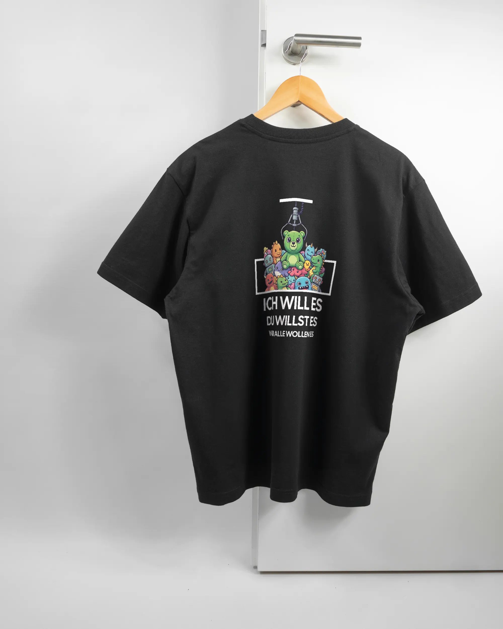 Rückseite des Basic Unisex T-Shirt Oversized von Maondo mit dem Design Will Stofftier in der Farbe Black und in der Größe S auf einem Bügel an der Türklinke aufgehängt