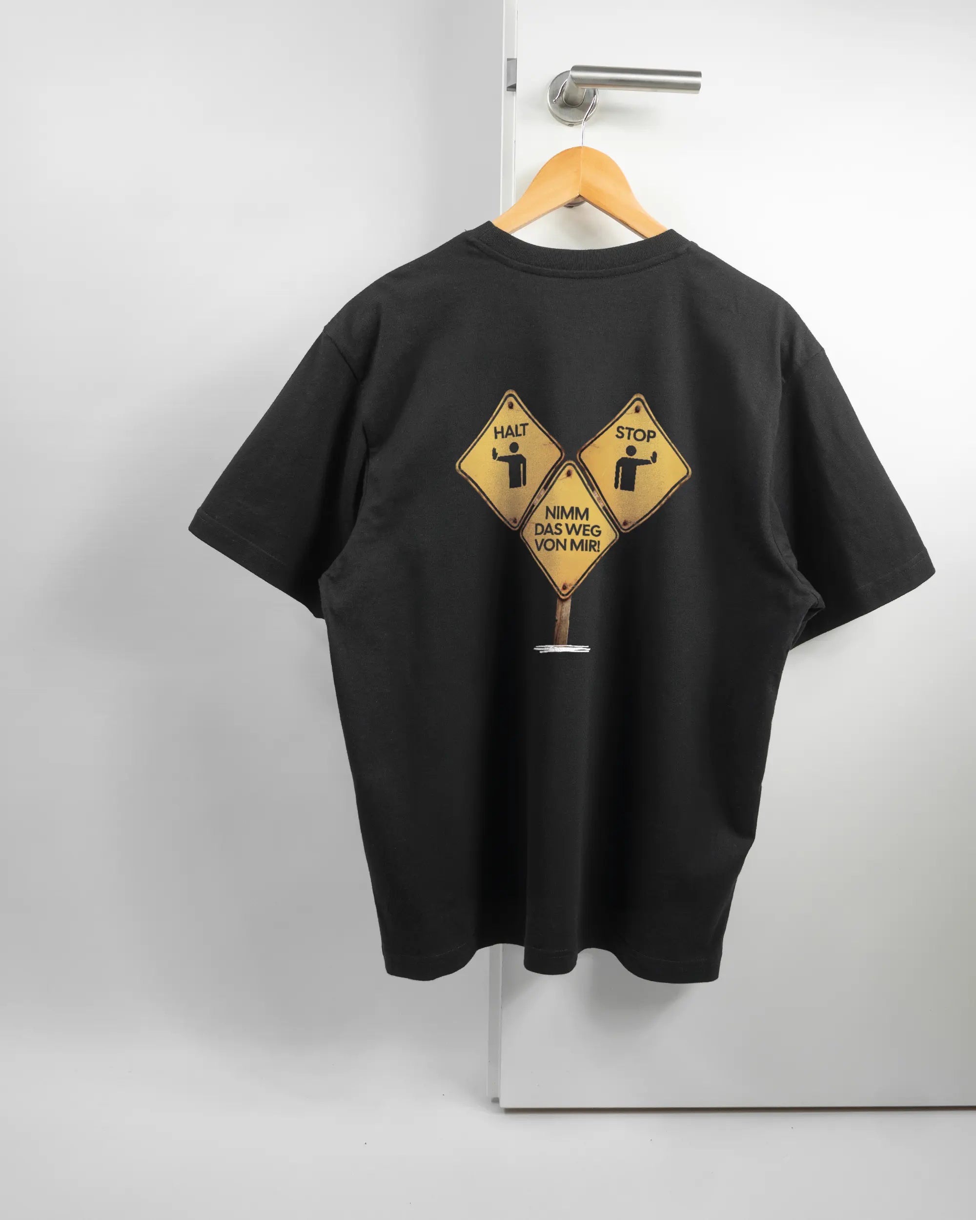 Rückseite des Basic Unisex T-Shirt Oversized von Maondo mit dem Design Schutzschild in der Farbe Black und in der Größe S auf einem Bügel an der Türklinke aufgehängt