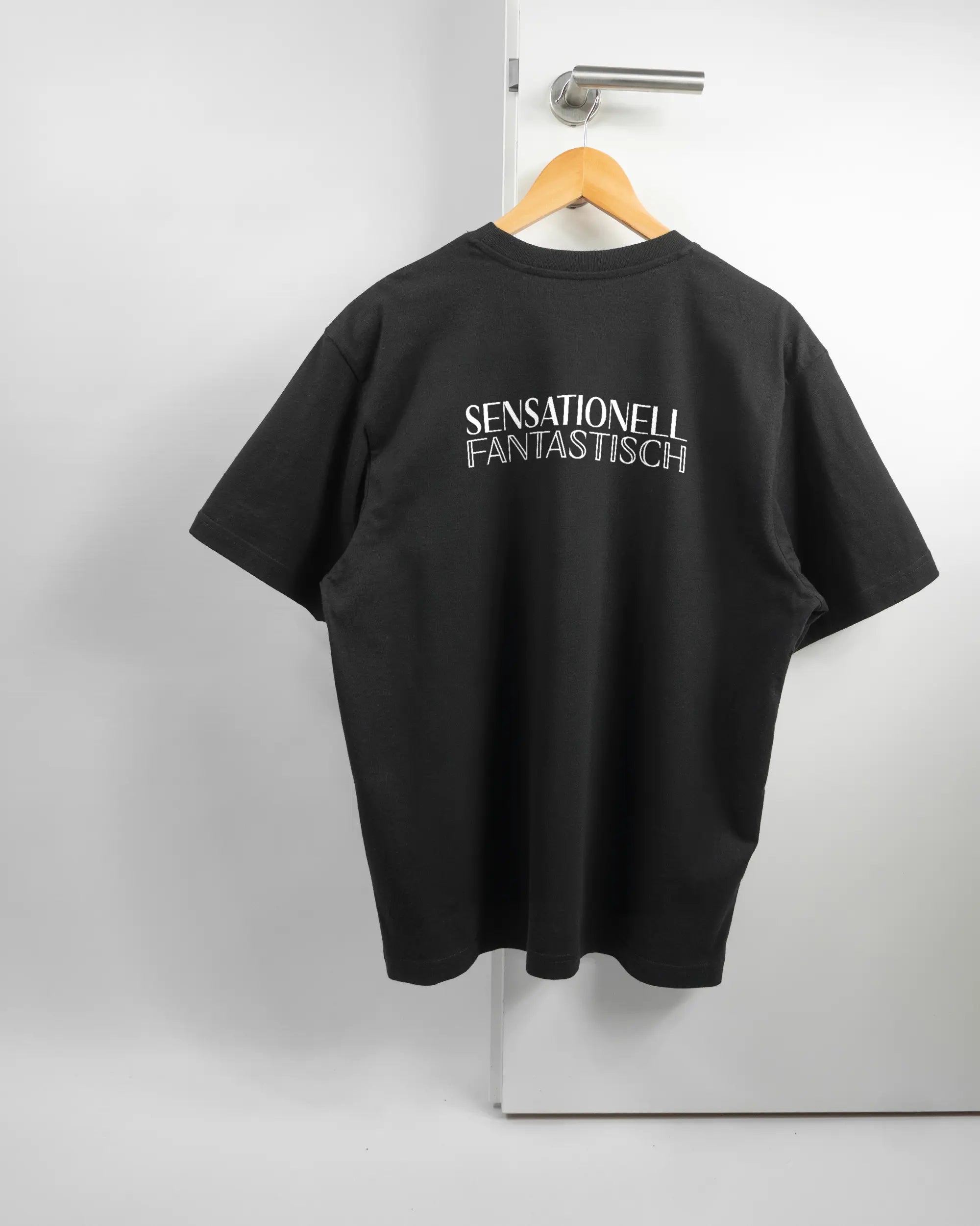 Rückseite des Basic Unisex T-Shirt Oversized von Maondo mit dem Design Sensationell in der Farbe Black und in der Größe S auf einem Bügel an der Türklinke aufgehängt