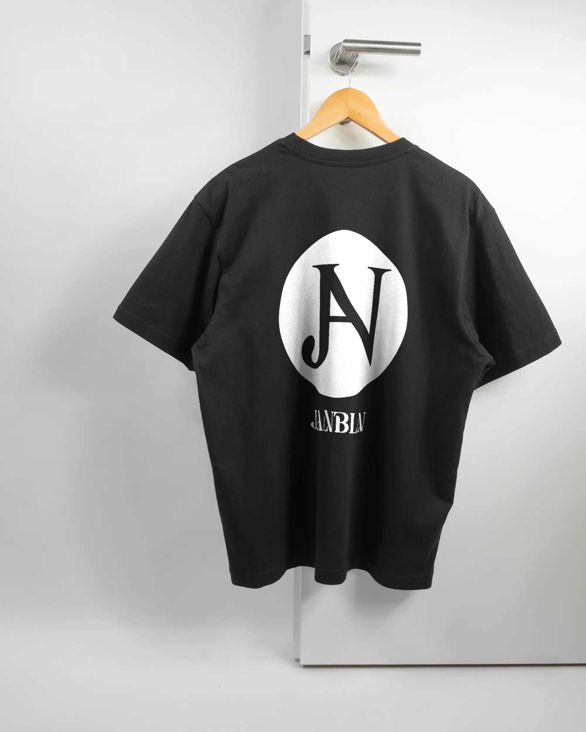 Rückseite des Basic Unisex T-Shirt Oversized von Maondo mit dem Design JB1 in der Farbe Black und in der Größe S auf einem Bügel an der Türklinke aufgehängt