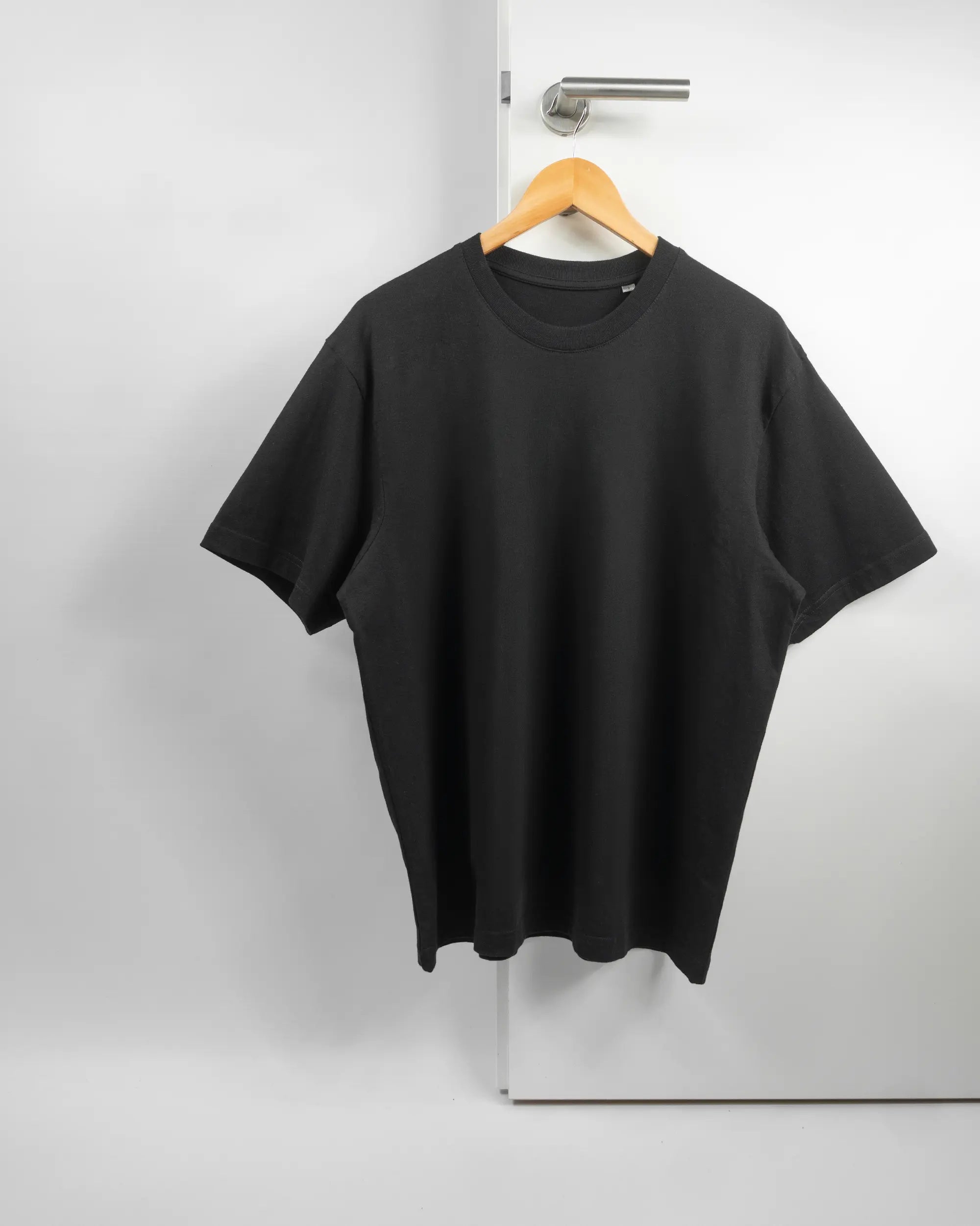Vorderseite des Basic Unisex T-Shirt Oversized von Maondo ohne Motiv in der Farbe Black und in der Größe S auf einem Bügel an der Türklinke aufgehängt