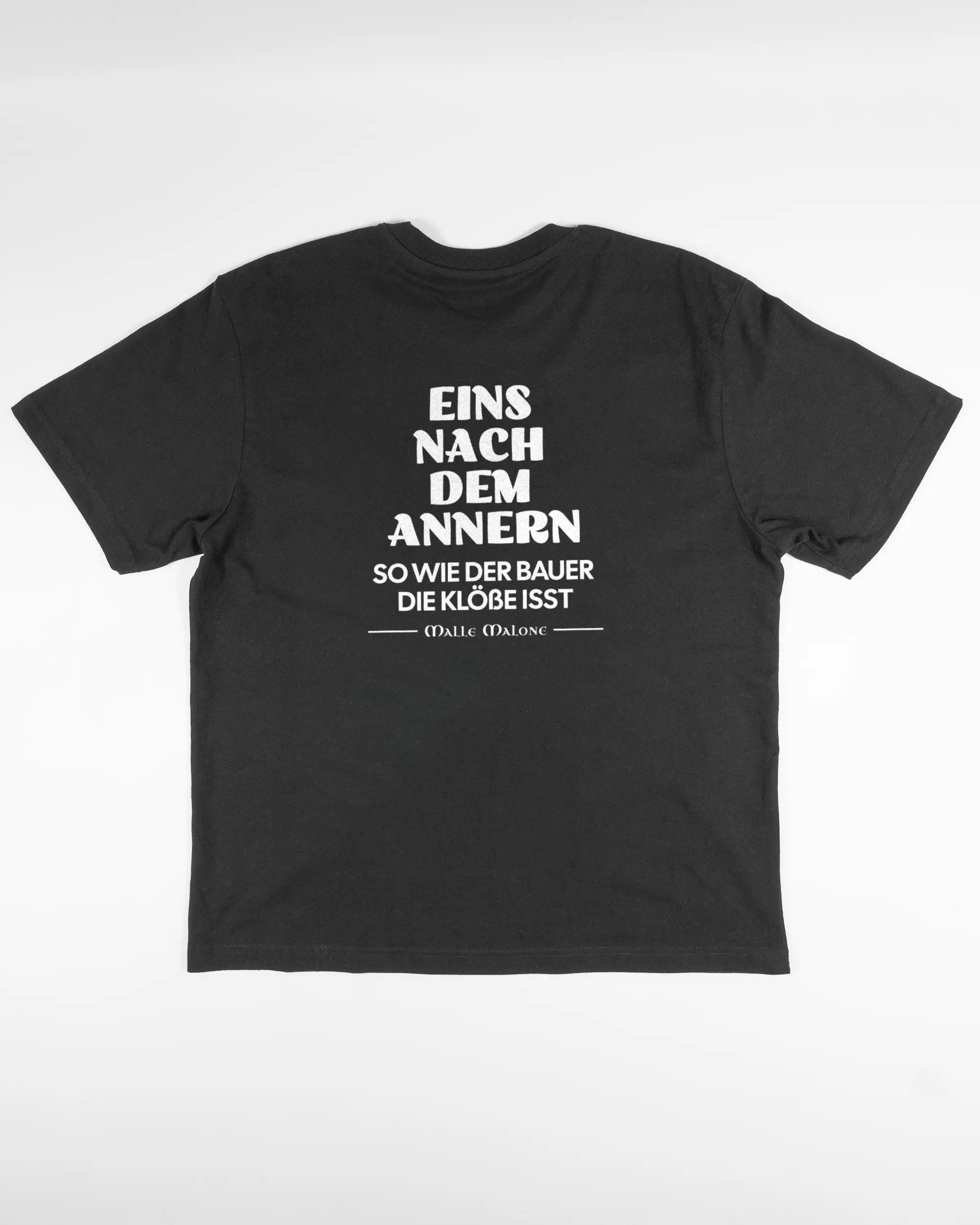 Rückseite des Basic Unisex T-Shirt Oversized von Maondo mit dem Design Eins nach dem Annern in der Farbe Black und in der Größe S flach auf den Boden gelegt