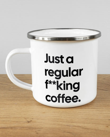 Titelbild, das die linke Seite der beidseitig bedruckten Emailletasse von Maondo mit dem Design Regular Coffee in der Farbe White-Silver auf einem Holztisch zeigt