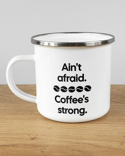 Titelbild, das die linke Seite der beidseitig bedruckten Emailletasse von Maondo mit dem Design Coffee is strong in der Farbe White-Silver auf einem Holztisch zeigt