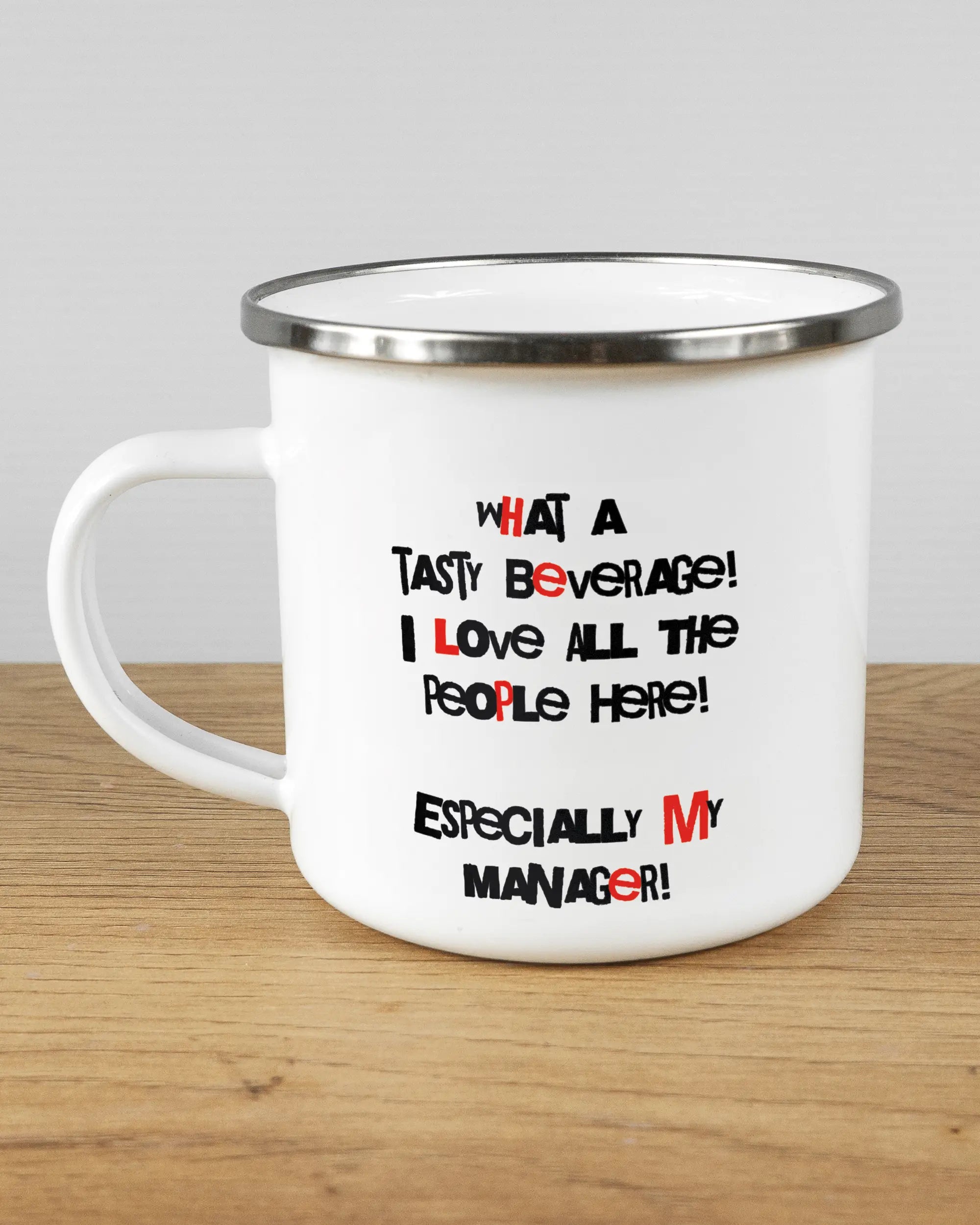 Titelbild, das die linke Seite der beidseitig bedruckten Emailletasse von Maondo mit dem Design Help me in der Farbe White-Silver auf einem Holztisch zeigt