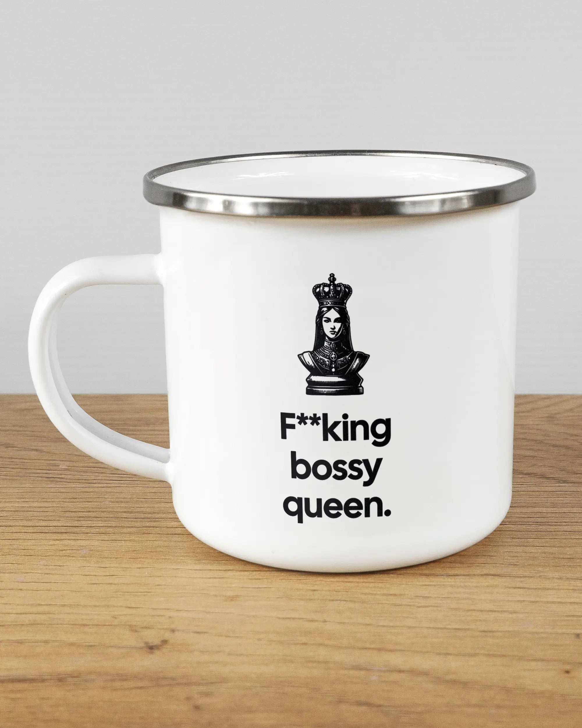 Titelbild, das die linke Seite der beidseitig bedruckten Emailletasse von Maondo mit dem Design Bossy Queen in der Farbe White-Silver auf einem Holztisch zeigt