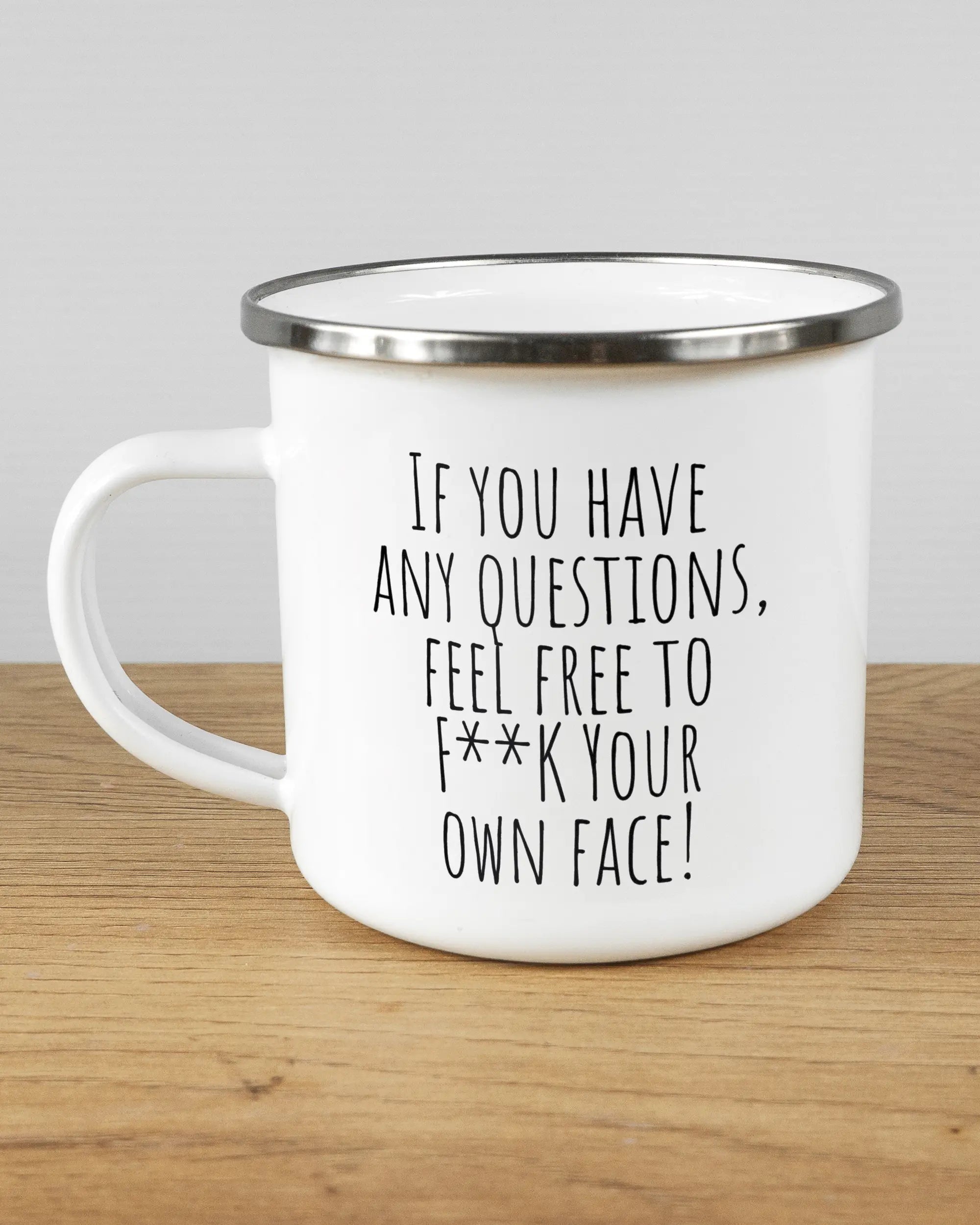 Titelbild, das die linke Seite der beidseitig bedruckten Emailletasse von Maondo mit dem Design Feel Free in der Farbe White-Silver auf einem Holztisch zeigt