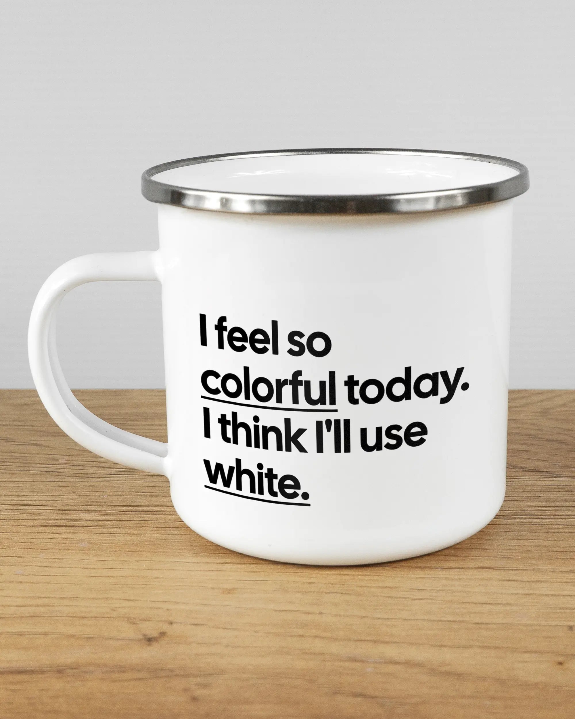 Titelbild, das die linke Seite der beidseitig bedruckten Emailletasse von Maondo mit dem Design Colorful Day in der Farbe White-Silver auf einem Holztisch zeigt