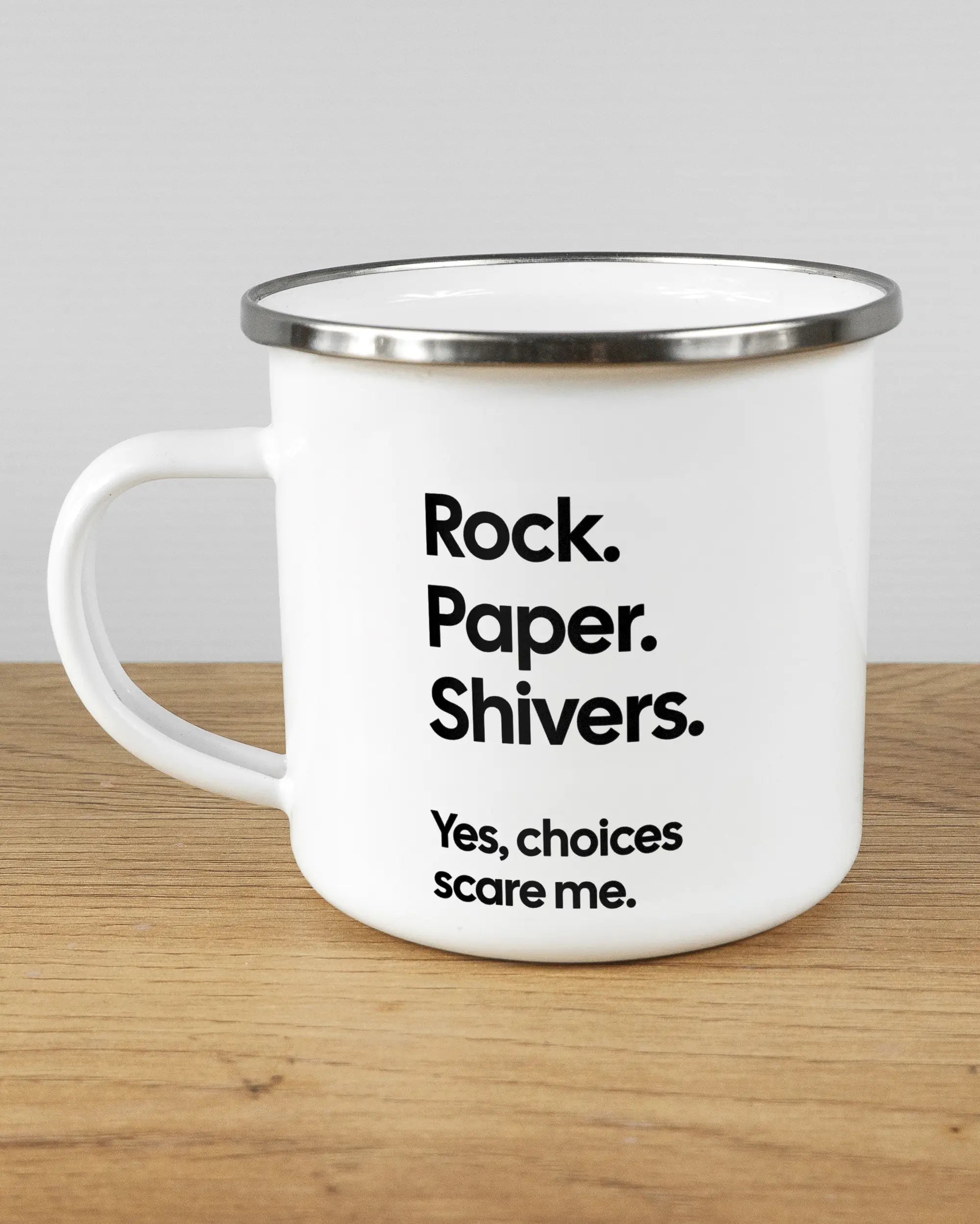 Titelbild, das die linke Seite der beidseitig bedruckten Emailletasse von Maondo mit dem Design Rock Paper Shivers in der Farbe White-Silver auf einem Holztisch zeigt