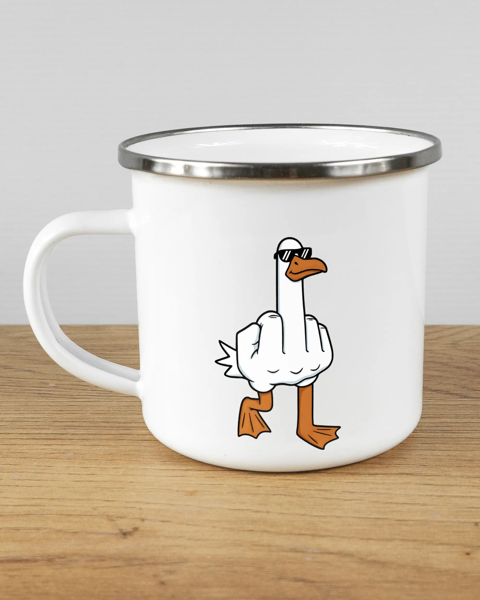 Titelbild, das die linke Seite der beidseitig bedruckten Emailletasse von Maondo mit dem Design I give a duck in der Farbe White-Silver auf einem Holztisch zeigt