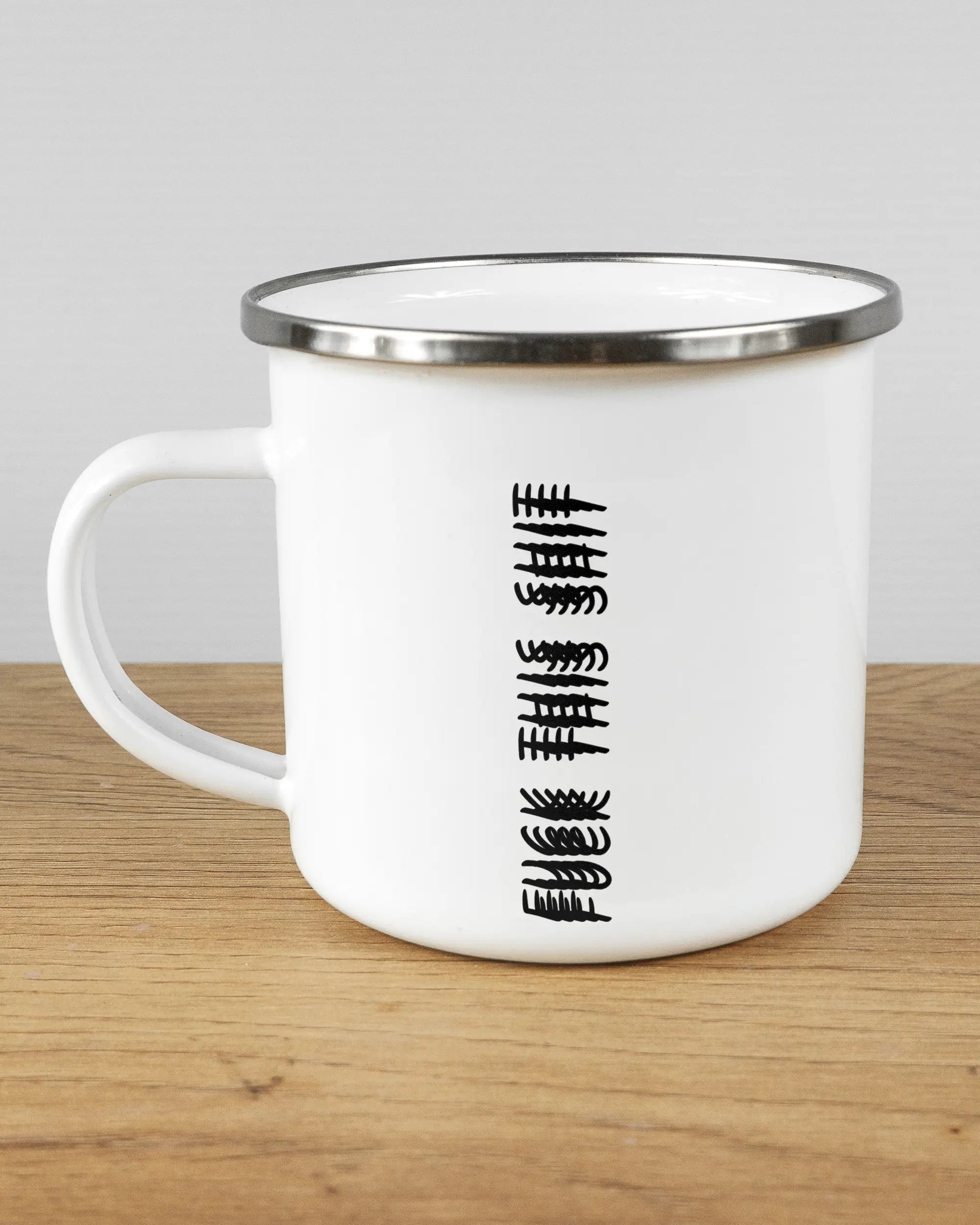 Titelbild, das die linke Seite der beidseitig bedruckten Emailletasse von Maondo mit dem Design Hidden Message in der Farbe White-Silver auf einem Holztisch zeigt