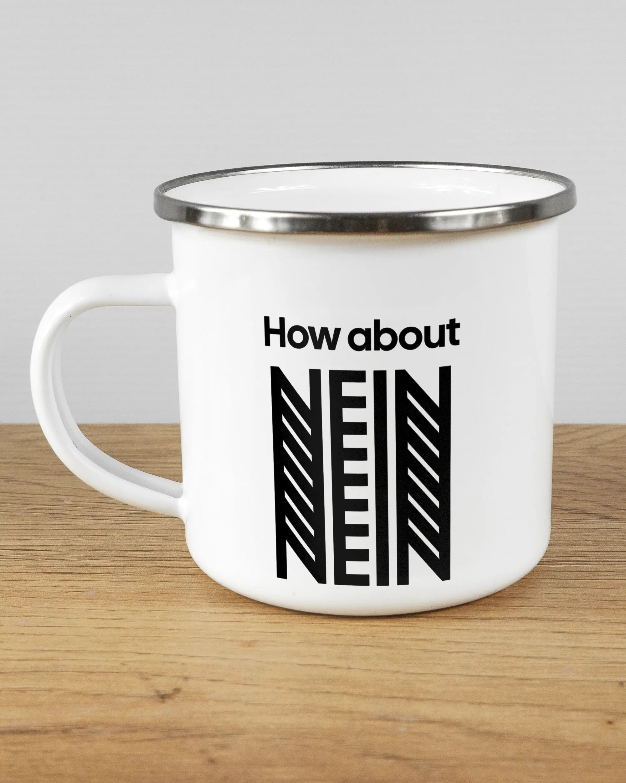 Titelbild, das die linke Seite der beidseitig bedruckten Emailletasse von Maondo mit dem Design How about nein in der Farbe White-Silver auf einem Holztisch zeigt